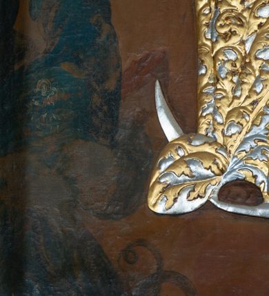 Zdjęcie nr 4: Obraz w formie stojącego prostokąta z przedstawieniem Matki Boskiej z Dzieciątkiem unoszącej się pomiędzy członkami bractwa i wiernymi. Maria ukazana jest w całej postaci, zwrócona frontalnie, z głową skierowaną w lewo, stoi na globie i na sierpie księżyca. Na lewym przedramieniu podtrzymuje Dzieciątko, w prawej dłoni trzyma berło. Maria ma pełną twarz, o okrągłych oczach i małym nosie, okoloną długimi, brązowymi włosami opadającymi wzdłuż ramion. W partii szat obraz przesłania płaskorzeźbiona sukienka, w postaci złoconej sukni o srebrzonym, akantowym wzorze oraz srebrzony płaszcz o złoconym, akantowym wzorze, narzucony na ramiona i podtrzymywany prawą ręką z przodu postaci. Maria ma na głowie płaskorzeźbioną koronę zamkniętą. Dzieciątko zwrócone jest w trzech czwartych w prawo, lewą ręką podtrzymuje jabłko królewskie, prawą błogosławi. Ma okrągłą twarz, o pełnych policzkach, okrągłych oczach skierowanych do góry, małym nosie i pełnych ustach, okoloną krótkimi, brązowymi włosami. W partii szat przesłonięte jest płaskorzeźbioną, złoconą sukienką o akantowym wzorze. Na głowie ma płaskorzeźbioną, zamkniętą koroną. Po prawej stronie Marii znajdują się dwie postacie członków bractwa w kapturach na głowach, z rękami złożonymi w geście modlitwy. Po lewej stronie Marii dwie postacie kobiece zwrócone w trzech czwartych, z rękami złożonymi w geście modlitwy. Postacie zostały ukazane na tle zachmurzonego brązowo-żółtego nieba, rozświetlonego wokół głowy Marii i Dzieciątka. W górnych narożach obraz dekorowany złoconym ornamentem rocaille&#039;owym z kwiatami. 