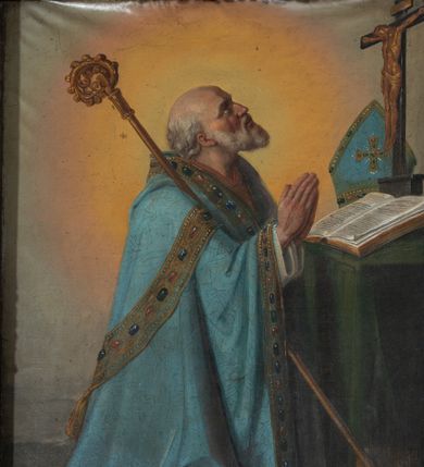 Zdjęcie nr 1: Obraz w formie stojącego prostokąta z przedstawieniem biskupa klęczącego przed stolikiem z krucyfiksem. Biskup zwrócony profilem w lewo, z uniesioną głową i dłońmi złożonymi w geście modlitwy. Twarz ma szczupłą, o starczych rysach, głęboko osadzonych oczach, skierowanych w górę, garbatym nosie i rozchylonych ustach z widocznymi zębami. Okolona jest siwą brodą i falowanymi włosami, na głowie ma łysinę. Ubrany jest w białą albę, niebieską, wzorzystą kapę, z dekoracyjną bordiurą z perłami i rautami, opadającą na ziemię. O jego prawe ramię oparty jest pastorał. Święty klęczy przed stołem nakrytym zieloną tkaniną, na nim leżą otwarta księga, krucyfiks i niebieska infuła. Obok stołu, na ziemi, zamknięta księga. Święty ukazany na szarym tle, rozświetlonym wokół jego postaci. 