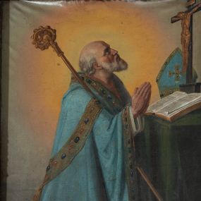 Zdjęcie nr 1: Obraz w formie stojącego prostokąta z przedstawieniem biskupa klęczącego przed stolikiem z krucyfiksem. Biskup zwrócony profilem w lewo, z uniesioną głową i dłońmi złożonymi w geście modlitwy. Twarz ma szczupłą, o starczych rysach, głęboko osadzonych oczach, skierowanych w górę, garbatym nosie i rozchylonych ustach z widocznymi zębami. Okolona jest siwą brodą i falowanymi włosami, na głowie ma łysinę. Ubrany jest w białą albę, niebieską, wzorzystą kapę, z dekoracyjną bordiurą z perłami i rautami, opadającą na ziemię. O jego prawe ramię oparty jest pastorał. Święty klęczy przed stołem nakrytym zieloną tkaniną, na nim leżą otwarta księga, krucyfiks i niebieska infuła. Obok stołu, na ziemi, zamknięta księga. Święty ukazany na szarym tle, rozświetlonym wokół jego postaci. 
