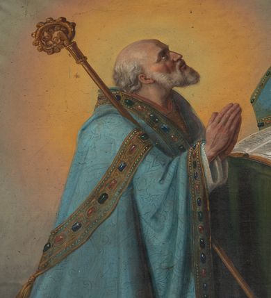 Zdjęcie nr 2: Obraz w formie stojącego prostokąta z przedstawieniem biskupa klęczącego przed stolikiem z krucyfiksem. Biskup zwrócony profilem w lewo, z uniesioną głową i dłońmi złożonymi w geście modlitwy. Twarz ma szczupłą, o starczych rysach, głęboko osadzonych oczach, skierowanych w górę, garbatym nosie i rozchylonych ustach z widocznymi zębami. Okolona jest siwą brodą i falowanymi włosami, na głowie ma łysinę. Ubrany jest w białą albę, niebieską, wzorzystą kapę, z dekoracyjną bordiurą z perłami i rautami, opadającą na ziemię. O jego prawe ramię oparty jest pastorał. Święty klęczy przed stołem nakrytym zieloną tkaniną, na nim leżą otwarta księga, krucyfiks i niebieska infuła. Obok stołu, na ziemi, zamknięta księga. Święty ukazany na szarym tle, rozświetlonym wokół jego postaci. 