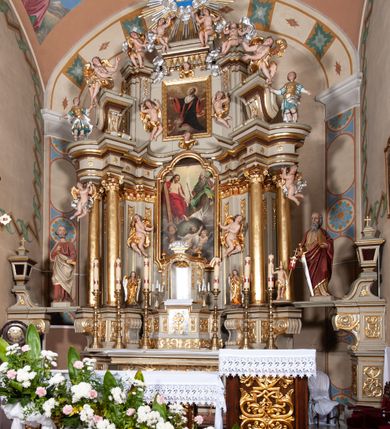 Zdjęcie nr 5: Nastawa architektoniczna, jednokondygnacyjna ze zwieńczeniem, jednoosiowa z bramkami. Ołtarz sarkofagowy z drewnianą mensą i portatylem. Na mensie znajduje się tabernakulum z tronem wystawienia. Tabernakulum w formie drewnianej skrzynki na planie wieloboku, ustawionej na cokole dekorowanym akantem, zamkniętej profilowaną listwą; ścianki dekorowane płycinami z akantem. Drzwiczki drewniane, obite blachą, w formie stojącego prostokąta, zdobione motywem krzyża, gorejącego serca, winnego grona i kłosów zboża. Tron wystawienia w formie obrotowej niszy, ujętej motywem winnego grona, flankowanej pilastrami dekorowanymi kampanulami, dźwigającymi gzyms zamykający całość, z wazonikami. Tron zwieńczony cokołem ze srebrzoną figurką leżącego baranka. 
Retabulum na dwustrefowym, uskokowym cokole ustawionym pod kątem, w górnej strefie z wyodrębnionymi po bokach postumentami i konsolami. Nastawa ujęta dwiema parami kolumn kompozytowych ustawionych na tle uskokowych, zwróconych pod kątem filarów, o trzonach dekorowanych płycinami z kampanulami. Podpory oraz dwa putta dźwigają wyłamane na ich osi, odcinkami wklęsło-wypukłe, pełne belkowanie, przerwane nad polem środkowym, z fryzem dekorowanym rozetami oraz fragmenty przerwanego, falistego przyczółka z siedzącymi na nim figurami aniołów. Na zewnętrznych krawędziach belkowania ustawione dwie figury w strojach żołnierzy. W polu środkowym nisza w formie stojącego prostokąta zamkniętego trójlistnie z uskokiem, o wklęsłych dolnych narożach, ujęta profilowaną ramą, z obrazem Trójcy Świętej i flankowana parą puttów. 
Zwieńczenie w formie stojącego prostokąta, flankowane parą zdwojonych pilastrów, zwróconych na zewnątrz, zamknięte odcinkiem gzymsu dekorowanym lambrekinem, ujęte obłokami z dwiema parami siedzących puttów. Powyżej medalion z okiem Opatrzności, ujętym obłokami i uskrzydlonymi główkami anielskimi, w glorii promienistej. W polu zwieńczenia obraz św. Jana Kantego w formie stojącego prostokąta, ujęty profilowaną ramą. 
Na wysokości cokołu nastawę flankują bramki utworzone przez postumenty przylegające do ścian prezbiterium zwieńczone fragmentami falistego przyczółka z latarniami. Cokoły przy ścianie z nastawą łączą listwy, tworząc przejścia, nad którymi stoją figury św. Piotra i św. Pawła. 
Struktura polichromowana w kolorze jasnozielonym, z brązowymi detalami, czerwonymi kapitelami; kolumny, ornamentyka i profile złocone, gloria i obłoki srebrzone. 

