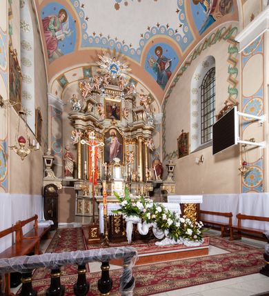 Zdjęcie nr 3: Nastawa architektoniczna, jednokondygnacyjna ze zwieńczeniem, jednoosiowa z bramkami. Ołtarz sarkofagowy z drewnianą mensą i portatylem. Na mensie znajduje się tabernakulum z tronem wystawienia. Tabernakulum w formie drewnianej skrzynki na planie wieloboku, ustawionej na cokole dekorowanym akantem, zamkniętej profilowaną listwą; ścianki dekorowane płycinami z akantem. Drzwiczki drewniane, obite blachą, w formie stojącego prostokąta, zdobione motywem krzyża, gorejącego serca, winnego grona i kłosów zboża. Tron wystawienia w formie obrotowej niszy, ujętej motywem winnego grona, flankowanej pilastrami dekorowanymi kampanulami, dźwigającymi gzyms zamykający całość, z wazonikami. Tron zwieńczony cokołem ze srebrzoną figurką leżącego baranka. 
Retabulum na dwustrefowym, uskokowym cokole ustawionym pod kątem, w górnej strefie z wyodrębnionymi po bokach postumentami i konsolami. Nastawa ujęta dwiema parami kolumn kompozytowych ustawionych na tle uskokowych, zwróconych pod kątem filarów, o trzonach dekorowanych płycinami z kampanulami. Podpory oraz dwa putta dźwigają wyłamane na ich osi, odcinkami wklęsło-wypukłe, pełne belkowanie, przerwane nad polem środkowym, z fryzem dekorowanym rozetami oraz fragmenty przerwanego, falistego przyczółka z siedzącymi na nim figurami aniołów. Na zewnętrznych krawędziach belkowania ustawione dwie figury w strojach żołnierzy. W polu środkowym nisza w formie stojącego prostokąta zamkniętego trójlistnie z uskokiem, o wklęsłych dolnych narożach, ujęta profilowaną ramą, z obrazem Trójcy Świętej i flankowana parą puttów. 
Zwieńczenie w formie stojącego prostokąta, flankowane parą zdwojonych pilastrów, zwróconych na zewnątrz, zamknięte odcinkiem gzymsu dekorowanym lambrekinem, ujęte obłokami z dwiema parami siedzących puttów. Powyżej medalion z okiem Opatrzności, ujętym obłokami i uskrzydlonymi główkami anielskimi, w glorii promienistej. W polu zwieńczenia obraz św. Jana Kantego w formie stojącego prostokąta, ujęty profilowaną ramą. 
Na wysokości cokołu nastawę flankują bramki utworzone przez postumenty przylegające do ścian prezbiterium zwieńczone fragmentami falistego przyczółka z latarniami. Cokoły przy ścianie z nastawą łączą listwy, tworząc przejścia, nad którymi stoją figury św. Piotra i św. Pawła. 
Struktura polichromowana w kolorze jasnozielonym, z brązowymi detalami, czerwonymi kapitelami; kolumny, ornamentyka i profile złocone, gloria i obłoki srebrzone. 

