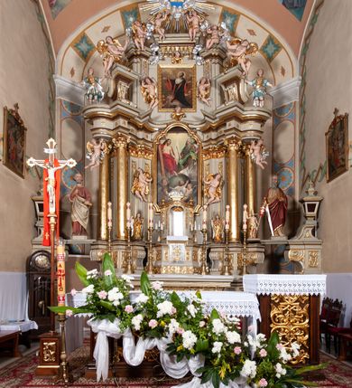 Zdjęcie nr 8: Nastawa architektoniczna, jednokondygnacyjna ze zwieńczeniem, jednoosiowa z bramkami. Ołtarz sarkofagowy z drewnianą mensą i portatylem. Na mensie znajduje się tabernakulum z tronem wystawienia. Tabernakulum w formie drewnianej skrzynki na planie wieloboku, ustawionej na cokole dekorowanym akantem, zamkniętej profilowaną listwą; ścianki dekorowane płycinami z akantem. Drzwiczki drewniane, obite blachą, w formie stojącego prostokąta, zdobione motywem krzyża, gorejącego serca, winnego grona i kłosów zboża. Tron wystawienia w formie obrotowej niszy, ujętej motywem winnego grona, flankowanej pilastrami dekorowanymi kampanulami, dźwigającymi gzyms zamykający całość, z wazonikami. Tron zwieńczony cokołem ze srebrzoną figurką leżącego baranka. 
Retabulum na dwustrefowym, uskokowym cokole ustawionym pod kątem, w górnej strefie z wyodrębnionymi po bokach postumentami i konsolami. Nastawa ujęta dwiema parami kolumn kompozytowych ustawionych na tle uskokowych, zwróconych pod kątem filarów, o trzonach dekorowanych płycinami z kampanulami. Podpory oraz dwa putta dźwigają wyłamane na ich osi, odcinkami wklęsło-wypukłe, pełne belkowanie, przerwane nad polem środkowym, z fryzem dekorowanym rozetami oraz fragmenty przerwanego, falistego przyczółka z siedzącymi na nim figurami aniołów. Na zewnętrznych krawędziach belkowania ustawione dwie figury w strojach żołnierzy. W polu środkowym nisza w formie stojącego prostokąta zamkniętego trójlistnie z uskokiem, o wklęsłych dolnych narożach, ujęta profilowaną ramą, z obrazem Trójcy Świętej i flankowana parą puttów. 
Zwieńczenie w formie stojącego prostokąta, flankowane parą zdwojonych pilastrów, zwróconych na zewnątrz, zamknięte odcinkiem gzymsu dekorowanym lambrekinem, ujęte obłokami z dwiema parami siedzących puttów. Powyżej medalion z okiem Opatrzności, ujętym obłokami i uskrzydlonymi główkami anielskimi, w glorii promienistej. W polu zwieńczenia obraz św. Jana Kantego w formie stojącego prostokąta, ujęty profilowaną ramą. 
Na wysokości cokołu nastawę flankują bramki utworzone przez postumenty przylegające do ścian prezbiterium zwieńczone fragmentami falistego przyczółka z latarniami. Cokoły przy ścianie z nastawą łączą listwy, tworząc przejścia, nad którymi stoją figury św. Piotra i św. Pawła. 
Struktura polichromowana w kolorze jasnozielonym, z brązowymi detalami, czerwonymi kapitelami; kolumny, ornamentyka i profile złocone, gloria i obłoki srebrzone. 

