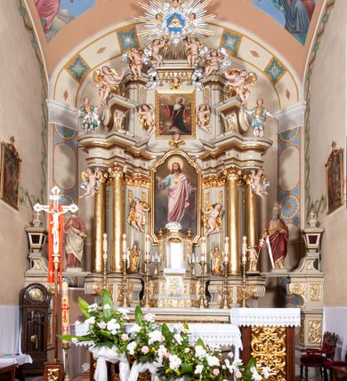 Zdjęcie nr 4: Nastawa architektoniczna, jednokondygnacyjna ze zwieńczeniem, jednoosiowa z bramkami. Ołtarz sarkofagowy z drewnianą mensą i portatylem. Na mensie znajduje się tabernakulum z tronem wystawienia. Tabernakulum w formie drewnianej skrzynki na planie wieloboku, ustawionej na cokole dekorowanym akantem, zamkniętej profilowaną listwą; ścianki dekorowane płycinami z akantem. Drzwiczki drewniane, obite blachą, w formie stojącego prostokąta, zdobione motywem krzyża, gorejącego serca, winnego grona i kłosów zboża. Tron wystawienia w formie obrotowej niszy, ujętej motywem winnego grona, flankowanej pilastrami dekorowanymi kampanulami, dźwigającymi gzyms zamykający całość, z wazonikami. Tron zwieńczony cokołem ze srebrzoną figurką leżącego baranka. 
Retabulum na dwustrefowym, uskokowym cokole ustawionym pod kątem, w górnej strefie z wyodrębnionymi po bokach postumentami i konsolami. Nastawa ujęta dwiema parami kolumn kompozytowych ustawionych na tle uskokowych, zwróconych pod kątem filarów, o trzonach dekorowanych płycinami z kampanulami. Podpory oraz dwa putta dźwigają wyłamane na ich osi, odcinkami wklęsło-wypukłe, pełne belkowanie, przerwane nad polem środkowym, z fryzem dekorowanym rozetami oraz fragmenty przerwanego, falistego przyczółka z siedzącymi na nim figurami aniołów. Na zewnętrznych krawędziach belkowania ustawione dwie figury w strojach żołnierzy. W polu środkowym nisza w formie stojącego prostokąta zamkniętego trójlistnie z uskokiem, o wklęsłych dolnych narożach, ujęta profilowaną ramą, z obrazem Trójcy Świętej i flankowana parą puttów. 
Zwieńczenie w formie stojącego prostokąta, flankowane parą zdwojonych pilastrów, zwróconych na zewnątrz, zamknięte odcinkiem gzymsu dekorowanym lambrekinem, ujęte obłokami z dwiema parami siedzących puttów. Powyżej medalion z okiem Opatrzności, ujętym obłokami i uskrzydlonymi główkami anielskimi, w glorii promienistej. W polu zwieńczenia obraz św. Jana Kantego w formie stojącego prostokąta, ujęty profilowaną ramą. 
Na wysokości cokołu nastawę flankują bramki utworzone przez postumenty przylegające do ścian prezbiterium zwieńczone fragmentami falistego przyczółka z latarniami. Cokoły przy ścianie z nastawą łączą listwy, tworząc przejścia, nad którymi stoją figury św. Piotra i św. Pawła. 
Struktura polichromowana w kolorze jasnozielonym, z brązowymi detalami, czerwonymi kapitelami; kolumny, ornamentyka i profile złocone, gloria i obłoki srebrzone. 

