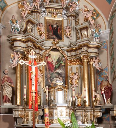 Zdjęcie nr 7: Nastawa architektoniczna, jednokondygnacyjna ze zwieńczeniem, jednoosiowa z bramkami. Ołtarz sarkofagowy z drewnianą mensą i portatylem. Na mensie znajduje się tabernakulum z tronem wystawienia. Tabernakulum w formie drewnianej skrzynki na planie wieloboku, ustawionej na cokole dekorowanym akantem, zamkniętej profilowaną listwą; ścianki dekorowane płycinami z akantem. Drzwiczki drewniane, obite blachą, w formie stojącego prostokąta, zdobione motywem krzyża, gorejącego serca, winnego grona i kłosów zboża. Tron wystawienia w formie obrotowej niszy, ujętej motywem winnego grona, flankowanej pilastrami dekorowanymi kampanulami, dźwigającymi gzyms zamykający całość, z wazonikami. Tron zwieńczony cokołem ze srebrzoną figurką leżącego baranka. 
Retabulum na dwustrefowym, uskokowym cokole ustawionym pod kątem, w górnej strefie z wyodrębnionymi po bokach postumentami i konsolami. Nastawa ujęta dwiema parami kolumn kompozytowych ustawionych na tle uskokowych, zwróconych pod kątem filarów, o trzonach dekorowanych płycinami z kampanulami. Podpory oraz dwa putta dźwigają wyłamane na ich osi, odcinkami wklęsło-wypukłe, pełne belkowanie, przerwane nad polem środkowym, z fryzem dekorowanym rozetami oraz fragmenty przerwanego, falistego przyczółka z siedzącymi na nim figurami aniołów. Na zewnętrznych krawędziach belkowania ustawione dwie figury w strojach żołnierzy. W polu środkowym nisza w formie stojącego prostokąta zamkniętego trójlistnie z uskokiem, o wklęsłych dolnych narożach, ujęta profilowaną ramą, z obrazem Trójcy Świętej i flankowana parą puttów. 
Zwieńczenie w formie stojącego prostokąta, flankowane parą zdwojonych pilastrów, zwróconych na zewnątrz, zamknięte odcinkiem gzymsu dekorowanym lambrekinem, ujęte obłokami z dwiema parami siedzących puttów. Powyżej medalion z okiem Opatrzności, ujętym obłokami i uskrzydlonymi główkami anielskimi, w glorii promienistej. W polu zwieńczenia obraz św. Jana Kantego w formie stojącego prostokąta, ujęty profilowaną ramą. 
Na wysokości cokołu nastawę flankują bramki utworzone przez postumenty przylegające do ścian prezbiterium zwieńczone fragmentami falistego przyczółka z latarniami. Cokoły przy ścianie z nastawą łączą listwy, tworząc przejścia, nad którymi stoją figury św. Piotra i św. Pawła. 
Struktura polichromowana w kolorze jasnozielonym, z brązowymi detalami, czerwonymi kapitelami; kolumny, ornamentyka i profile złocone, gloria i obłoki srebrzone. 

