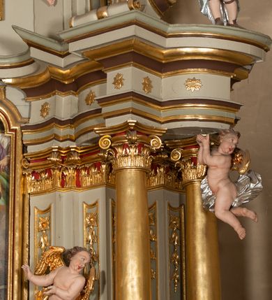 Zdjęcie nr 15: Nastawa architektoniczna, jednokondygnacyjna ze zwieńczeniem, jednoosiowa z bramkami. Ołtarz sarkofagowy z drewnianą mensą i portatylem. Na mensie znajduje się tabernakulum z tronem wystawienia. Tabernakulum w formie drewnianej skrzynki na planie wieloboku, ustawionej na cokole dekorowanym akantem, zamkniętej profilowaną listwą; ścianki dekorowane płycinami z akantem. Drzwiczki drewniane, obite blachą, w formie stojącego prostokąta, zdobione motywem krzyża, gorejącego serca, winnego grona i kłosów zboża. Tron wystawienia w formie obrotowej niszy, ujętej motywem winnego grona, flankowanej pilastrami dekorowanymi kampanulami, dźwigającymi gzyms zamykający całość, z wazonikami. Tron zwieńczony cokołem ze srebrzoną figurką leżącego baranka. 
Retabulum na dwustrefowym, uskokowym cokole ustawionym pod kątem, w górnej strefie z wyodrębnionymi po bokach postumentami i konsolami. Nastawa ujęta dwiema parami kolumn kompozytowych ustawionych na tle uskokowych, zwróconych pod kątem filarów, o trzonach dekorowanych płycinami z kampanulami. Podpory oraz dwa putta dźwigają wyłamane na ich osi, odcinkami wklęsło-wypukłe, pełne belkowanie, przerwane nad polem środkowym, z fryzem dekorowanym rozetami oraz fragmenty przerwanego, falistego przyczółka z siedzącymi na nim figurami aniołów. Na zewnętrznych krawędziach belkowania ustawione dwie figury w strojach żołnierzy. W polu środkowym nisza w formie stojącego prostokąta zamkniętego trójlistnie z uskokiem, o wklęsłych dolnych narożach, ujęta profilowaną ramą, z obrazem Trójcy Świętej i flankowana parą puttów. 
Zwieńczenie w formie stojącego prostokąta, flankowane parą zdwojonych pilastrów, zwróconych na zewnątrz, zamknięte odcinkiem gzymsu dekorowanym lambrekinem, ujęte obłokami z dwiema parami siedzących puttów. Powyżej medalion z okiem Opatrzności, ujętym obłokami i uskrzydlonymi główkami anielskimi, w glorii promienistej. W polu zwieńczenia obraz św. Jana Kantego w formie stojącego prostokąta, ujęty profilowaną ramą. 
Na wysokości cokołu nastawę flankują bramki utworzone przez postumenty przylegające do ścian prezbiterium zwieńczone fragmentami falistego przyczółka z latarniami. Cokoły przy ścianie z nastawą łączą listwy, tworząc przejścia, nad którymi stoją figury św. Piotra i św. Pawła. 
Struktura polichromowana w kolorze jasnozielonym, z brązowymi detalami, czerwonymi kapitelami; kolumny, ornamentyka i profile złocone, gloria i obłoki srebrzone. 

