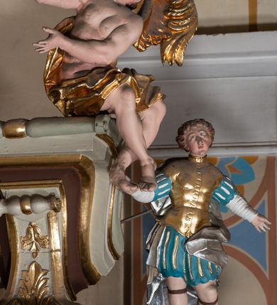 Zdjęcie nr 16: Nastawa architektoniczna, jednokondygnacyjna ze zwieńczeniem, jednoosiowa z bramkami. Ołtarz sarkofagowy z drewnianą mensą i portatylem. Na mensie znajduje się tabernakulum z tronem wystawienia. Tabernakulum w formie drewnianej skrzynki na planie wieloboku, ustawionej na cokole dekorowanym akantem, zamkniętej profilowaną listwą; ścianki dekorowane płycinami z akantem. Drzwiczki drewniane, obite blachą, w formie stojącego prostokąta, zdobione motywem krzyża, gorejącego serca, winnego grona i kłosów zboża. Tron wystawienia w formie obrotowej niszy, ujętej motywem winnego grona, flankowanej pilastrami dekorowanymi kampanulami, dźwigającymi gzyms zamykający całość, z wazonikami. Tron zwieńczony cokołem ze srebrzoną figurką leżącego baranka. 
Retabulum na dwustrefowym, uskokowym cokole ustawionym pod kątem, w górnej strefie z wyodrębnionymi po bokach postumentami i konsolami. Nastawa ujęta dwiema parami kolumn kompozytowych ustawionych na tle uskokowych, zwróconych pod kątem filarów, o trzonach dekorowanych płycinami z kampanulami. Podpory oraz dwa putta dźwigają wyłamane na ich osi, odcinkami wklęsło-wypukłe, pełne belkowanie, przerwane nad polem środkowym, z fryzem dekorowanym rozetami oraz fragmenty przerwanego, falistego przyczółka z siedzącymi na nim figurami aniołów. Na zewnętrznych krawędziach belkowania ustawione dwie figury w strojach żołnierzy. W polu środkowym nisza w formie stojącego prostokąta zamkniętego trójlistnie z uskokiem, o wklęsłych dolnych narożach, ujęta profilowaną ramą, z obrazem Trójcy Świętej i flankowana parą puttów. 
Zwieńczenie w formie stojącego prostokąta, flankowane parą zdwojonych pilastrów, zwróconych na zewnątrz, zamknięte odcinkiem gzymsu dekorowanym lambrekinem, ujęte obłokami z dwiema parami siedzących puttów. Powyżej medalion z okiem Opatrzności, ujętym obłokami i uskrzydlonymi główkami anielskimi, w glorii promienistej. W polu zwieńczenia obraz św. Jana Kantego w formie stojącego prostokąta, ujęty profilowaną ramą. 
Na wysokości cokołu nastawę flankują bramki utworzone przez postumenty przylegające do ścian prezbiterium zwieńczone fragmentami falistego przyczółka z latarniami. Cokoły przy ścianie z nastawą łączą listwy, tworząc przejścia, nad którymi stoją figury św. Piotra i św. Pawła. 
Struktura polichromowana w kolorze jasnozielonym, z brązowymi detalami, czerwonymi kapitelami; kolumny, ornamentyka i profile złocone, gloria i obłoki srebrzone. 

