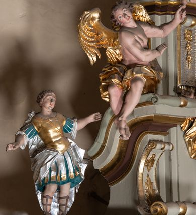 Zdjęcie nr 24: Nastawa architektoniczna, jednokondygnacyjna ze zwieńczeniem, jednoosiowa z bramkami. Ołtarz sarkofagowy z drewnianą mensą i portatylem. Na mensie znajduje się tabernakulum z tronem wystawienia. Tabernakulum w formie drewnianej skrzynki na planie wieloboku, ustawionej na cokole dekorowanym akantem, zamkniętej profilowaną listwą; ścianki dekorowane płycinami z akantem. Drzwiczki drewniane, obite blachą, w formie stojącego prostokąta, zdobione motywem krzyża, gorejącego serca, winnego grona i kłosów zboża. Tron wystawienia w formie obrotowej niszy, ujętej motywem winnego grona, flankowanej pilastrami dekorowanymi kampanulami, dźwigającymi gzyms zamykający całość, z wazonikami. Tron zwieńczony cokołem ze srebrzoną figurką leżącego baranka. 
Retabulum na dwustrefowym, uskokowym cokole ustawionym pod kątem, w górnej strefie z wyodrębnionymi po bokach postumentami i konsolami. Nastawa ujęta dwiema parami kolumn kompozytowych ustawionych na tle uskokowych, zwróconych pod kątem filarów, o trzonach dekorowanych płycinami z kampanulami. Podpory oraz dwa putta dźwigają wyłamane na ich osi, odcinkami wklęsło-wypukłe, pełne belkowanie, przerwane nad polem środkowym, z fryzem dekorowanym rozetami oraz fragmenty przerwanego, falistego przyczółka z siedzącymi na nim figurami aniołów. Na zewnętrznych krawędziach belkowania ustawione dwie figury w strojach żołnierzy. W polu środkowym nisza w formie stojącego prostokąta zamkniętego trójlistnie z uskokiem, o wklęsłych dolnych narożach, ujęta profilowaną ramą, z obrazem Trójcy Świętej i flankowana parą puttów. 
Zwieńczenie w formie stojącego prostokąta, flankowane parą zdwojonych pilastrów, zwróconych na zewnątrz, zamknięte odcinkiem gzymsu dekorowanym lambrekinem, ujęte obłokami z dwiema parami siedzących puttów. Powyżej medalion z okiem Opatrzności, ujętym obłokami i uskrzydlonymi główkami anielskimi, w glorii promienistej. W polu zwieńczenia obraz św. Jana Kantego w formie stojącego prostokąta, ujęty profilowaną ramą. 
Na wysokości cokołu nastawę flankują bramki utworzone przez postumenty przylegające do ścian prezbiterium zwieńczone fragmentami falistego przyczółka z latarniami. Cokoły przy ścianie z nastawą łączą listwy, tworząc przejścia, nad którymi stoją figury św. Piotra i św. Pawła. 
Struktura polichromowana w kolorze jasnozielonym, z brązowymi detalami, czerwonymi kapitelami; kolumny, ornamentyka i profile złocone, gloria i obłoki srebrzone. 

