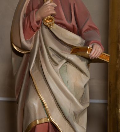 Zdjęcie nr 3: Rzeźba drążona z tyłu, ustawiona na podstawie na planie kwadratu o ściętych narożach. Święty ukazany jest w całej postaci, zwrócony frontalnie, z głową skierowaną w lewo, w kontrapoście. Lewą ręką trzyma przy boku księgę, prawą z kluczami w dłoni kładzie na piersi. Twarz ma pociągłą, o głęboko osadzonych oczach, uniesionych brwiach, dużym nosie i pełnych ustach, okoloną krótką, gęstą brodą oraz siwymi, krótkimi włosami z kosmykiem nad czołem. Ubrany jest w długą, czerwoną tunikę ze złoconą lamówką oraz osłaniający prawe ramię i zawinięty wokół postaci szary płaszcz ze złotą lamówką. Polichromia naturalistyczna w partiach ciała. 