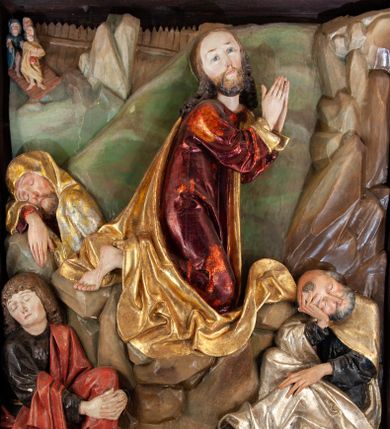 Zdjęcie nr 1: Płaskorzeźba o głębokim reliefie, w formie stojącego prostokąta z przedstawieniem modlącego się na skale Chrystusa w otoczeniu trzech śpiących apostołów. W centrum kompozycji postać klęczącego Chrystusa, zwróconego w trzech czwartych w lewo, z głową skierowaną niemal frontalnie oraz z dłońmi złożonymi w geście modlitwy. Twarz ma owalną, o wysokim czole, wąskich, oczach i nosie, małych ustach, okoloną krótką brodą i włosami rzeźbionymi w silnie skręcone pukle opadające na ramiona. Ubrany jest w luźną, laserowaną na czerwono tunikę, o szerokich, odwiniętych rękawach oraz złoty płaszcz zarzucony na lewy bok postaci, opadający z tyłu na nogi i z przodu na ziemię, silnie drapowany w łamane i misowe fałdy. Na pierwszym planie, w lewym dolnym rogu św. Jan ukazany jako śpiący, siedzący na lewej nodze, z ugiętą prawą przytrzymywaną obiema rękami przy korpusie, zwrócony jest w trzech czwartych w lewo, z głową opadającą na prawy bark. Twarz ma kwadratową, o zamkniętych, migdałowatych oczach, wąskim nosie i małych ustach, okoloną silnie kręconymi w rurkowate pukle włosami, sięgającymi ramion, z grzywką. Ubrany jest w czarną, luźną tunikę oraz czerwony płaszcz zarzucony na lewe ramię i zawinięty wokół nóg, przylegający do ciała. W prawym dolnym rogu śpiący św. Piotr, ukazany jako siedzący, z wysunięta do przodu lewą nogą, na prawej opiera łokieć ręki podtrzymującej jego opadającą głowę, lewa ręka spoczywa na kolanie. Zwrócony jest w trzech czwartych w prawo, z głową skierowana w przeciwną stronę. Twarz ma kwadratową, o zamkniętych, migdałowatych oczach, wąskim nosie i małych ustach, okoloną krótką, siwą silnie kręconą brodą oraz krótkimi włosami, z łysiną na głowie. Ubrany jest w granatową, luźną tunikę i srebrny płaszcz zarzucony na ramiona, zapięty pod szyją i opadający na nogi. Na trzecim planie, za skałą nad św. Janem wyłania się półpostać śpiącego św. Jakuba, opartego prawą ręką na skale, na której spoczywa jego głowa. Twarz ma kwadratową, o zamkniętych, migdałowatych oczach, wąskim nosie i małych ustach, okoloną krótką, brązową, silnie kręconą brodą. Ubrany jest w czerwoną, laserowaną tunikę i złocony płaszcz zarzucony na głowę i ramiona. W oddali, w lewym górnym rogu przy sztachetowym płocie widoczne są niewielkie trzy postacie Judasza i żołnierzy idących mostkiem. Tło w postaci zielonych pól. Płaskorzeźba ujęta profilowaną ramą. U spodu przedstawienia napis „Renovatum 1856 / Pinxyt Sitarski”.
