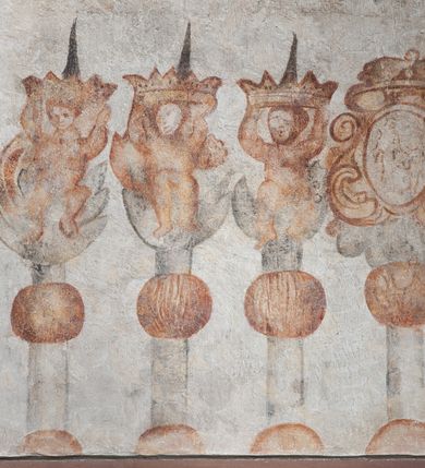 Zdjęcie nr 3: Na ścianie bocznej nawy odkryte dwa panele w formie stojącego prostokąta z fragmentami polichromii. Pierwszy panel z fragmentem sceny procesji, ze stojącymi, pochylonymi i leżącymi postaciami, ujętej w kartusz utworzony z esownic, cęg i elementów dekoracji roślinnej. Poniżej zacheuszek z namalowanym krzyżem w wieńcu laurowym. Pod nim malowana rama stacji drogi krzyżowej w formie stojącego prostokąta, ujętego ornamentem, z owalnym kartuszem w górnej części z napisem „STACYA IX” oraz fantazyjnym kartuszem u dołu z napisem „Jezus trzeci raz pod / krzyżem upada”. Obok ramy malowane trzy lichtarze z profitkami podtrzymywanymi przez putta oraz latarnia (?). Drugi panel z namalowanym medalionem z monogramem Marii w polu, w glorii promienistej, w otoku z róż. Pod nim esowate ornamenty, przyjmujące formy roślinne. 