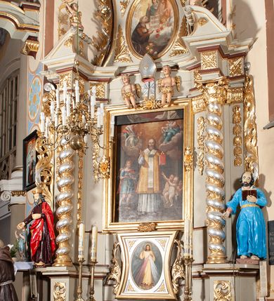 Zdjęcie nr 2: Nastawa architektoniczna, jednoosiowa, jednokondygnacyjna ze zwieńczeniem, ustawiona na cokole z wyodrębnionymi po bokach dwoma postumentami. Ołtarz prostopadłościenny z drewnianą mensą, z portatylem. Antepedium z kwiecistej tkaniny, z wyhaftowanym monogramem IHS w centrum, ujęte profilowaną ramą. Nastawa flankowana parą kolumn o skręconych trzonach i kapitelach kompozytowych stojących na tle dwóch par pilastrów o trzonach dekorowanych kampanulami. Podpory dźwigają pełne belkowanie, wyłamane na ich osi, przerwane nad polem środkowym, z fryzem dekorowanym rozetami oraz fragmenty przerwanego, falistego przyczółka ozdobionego kampanulami z parą puttów. Po zewnętrznej stronie kolumn, na wspornikach stoją figury św. Augustyna i św. Jana Kantego. W polu środkowym nisza w formie stojącego prostokąta z obrazem św. Mikołaja w profilowanej ramie. Nad polem środkowym dwa putta trzymające kwiaty, pomiędzy nimi infuła. Nastawa flankowana uszami utworzonymi z akantu przeplatanego wstęgą regencyjną. Zwieńczenie w formie pionowego prostokąta, o wklęsłych bokach, zamkniętego odcinkiem gzymsu wyłamanym w łuk ostry, ujęte liśćmi palmowymi z wstęgą. Całość zamknięta medalionem z gołębicą Ducha Świętego wśród obłoków i uskrzydlonych główek anielskich, w glorii promienistej. W polu obraz przedstawiający św. Franciszka przed Jezusem i Marią w formie stojącego owalu, w profilowanej ramie. Pole zwieńczenia wypełnione ornamentem roślinnym. Struktura architektoniczna polichromowana w kolorze jasnozielonym, kolumny, ornamentyka i profile złocone i srebrzone. 