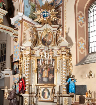 Zdjęcie nr 1: Nastawa architektoniczna, jednoosiowa, jednokondygnacyjna ze zwieńczeniem, ustawiona na cokole z wyodrębnionymi po bokach dwoma postumentami. Ołtarz prostopadłościenny z drewnianą mensą, z portatylem. Antepedium z kwiecistej tkaniny, z wyhaftowanym monogramem IHS w centrum, ujęte profilowaną ramą. Nastawa flankowana parą kolumn o skręconych trzonach i kapitelach kompozytowych stojących na tle dwóch par pilastrów o trzonach dekorowanych kampanulami. Podpory dźwigają pełne belkowanie, wyłamane na ich osi, przerwane nad polem środkowym, z fryzem dekorowanym rozetami oraz fragmenty przerwanego, falistego przyczółka ozdobionego kampanulami z parą puttów. Po zewnętrznej stronie kolumn, na wspornikach stoją figury św. Augustyna i św. Jana Kantego. W polu środkowym nisza w formie stojącego prostokąta z obrazem św. Mikołaja w profilowanej ramie. Nad polem środkowym dwa putta trzymające kwiaty, pomiędzy nimi infuła. Nastawa flankowana uszami utworzonymi z akantu przeplatanego wstęgą regencyjną. Zwieńczenie w formie pionowego prostokąta, o wklęsłych bokach, zamkniętego odcinkiem gzymsu wyłamanym w łuk ostry, ujęte liśćmi palmowymi z wstęgą. Całość zamknięta medalionem z gołębicą Ducha Świętego wśród obłoków i uskrzydlonych główek anielskich, w glorii promienistej. W polu obraz przedstawiający św. Franciszka przed Jezusem i Marią w formie stojącego owalu, w profilowanej ramie. Pole zwieńczenia wypełnione ornamentem roślinnym. Struktura architektoniczna polichromowana w kolorze jasnozielonym, kolumny, ornamentyka i profile złocone i srebrzone. 