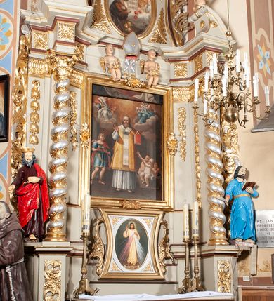 Zdjęcie nr 4: Nastawa architektoniczna, jednoosiowa, jednokondygnacyjna ze zwieńczeniem, ustawiona na cokole z wyodrębnionymi po bokach dwoma postumentami. Ołtarz prostopadłościenny z drewnianą mensą, z portatylem. Antepedium z kwiecistej tkaniny, z wyhaftowanym monogramem IHS w centrum, ujęte profilowaną ramą. Nastawa flankowana parą kolumn o skręconych trzonach i kapitelach kompozytowych stojących na tle dwóch par pilastrów o trzonach dekorowanych kampanulami. Podpory dźwigają pełne belkowanie, wyłamane na ich osi, przerwane nad polem środkowym, z fryzem dekorowanym rozetami oraz fragmenty przerwanego, falistego przyczółka ozdobionego kampanulami z parą puttów. Po zewnętrznej stronie kolumn, na wspornikach stoją figury św. Augustyna i św. Jana Kantego. W polu środkowym nisza w formie stojącego prostokąta z obrazem św. Mikołaja w profilowanej ramie. Nad polem środkowym dwa putta trzymające kwiaty, pomiędzy nimi infuła. Nastawa flankowana uszami utworzonymi z akantu przeplatanego wstęgą regencyjną. Zwieńczenie w formie pionowego prostokąta, o wklęsłych bokach, zamkniętego odcinkiem gzymsu wyłamanym w łuk ostry, ujęte liśćmi palmowymi z wstęgą. Całość zamknięta medalionem z gołębicą Ducha Świętego wśród obłoków i uskrzydlonych główek anielskich, w glorii promienistej. W polu obraz przedstawiający św. Franciszka przed Jezusem i Marią w formie stojącego owalu, w profilowanej ramie. Pole zwieńczenia wypełnione ornamentem roślinnym. Struktura architektoniczna polichromowana w kolorze jasnozielonym, kolumny, ornamentyka i profile złocone i srebrzone. 