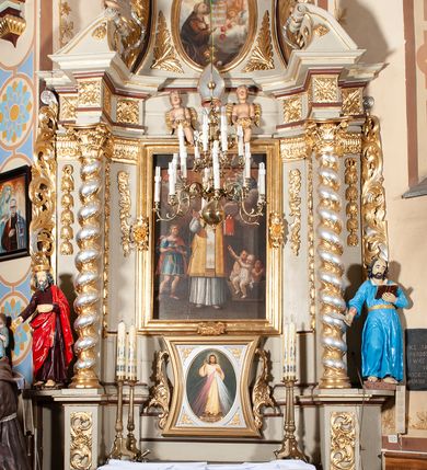 Zdjęcie nr 3: Nastawa architektoniczna, jednoosiowa, jednokondygnacyjna ze zwieńczeniem, ustawiona na cokole z wyodrębnionymi po bokach dwoma postumentami. Ołtarz prostopadłościenny z drewnianą mensą, z portatylem. Antepedium z kwiecistej tkaniny, z wyhaftowanym monogramem IHS w centrum, ujęte profilowaną ramą. Nastawa flankowana parą kolumn o skręconych trzonach i kapitelach kompozytowych stojących na tle dwóch par pilastrów o trzonach dekorowanych kampanulami. Podpory dźwigają pełne belkowanie, wyłamane na ich osi, przerwane nad polem środkowym, z fryzem dekorowanym rozetami oraz fragmenty przerwanego, falistego przyczółka ozdobionego kampanulami z parą puttów. Po zewnętrznej stronie kolumn, na wspornikach stoją figury św. Augustyna i św. Jana Kantego. W polu środkowym nisza w formie stojącego prostokąta z obrazem św. Mikołaja w profilowanej ramie. Nad polem środkowym dwa putta trzymające kwiaty, pomiędzy nimi infuła. Nastawa flankowana uszami utworzonymi z akantu przeplatanego wstęgą regencyjną. Zwieńczenie w formie pionowego prostokąta, o wklęsłych bokach, zamkniętego odcinkiem gzymsu wyłamanym w łuk ostry, ujęte liśćmi palmowymi z wstęgą. Całość zamknięta medalionem z gołębicą Ducha Świętego wśród obłoków i uskrzydlonych główek anielskich, w glorii promienistej. W polu obraz przedstawiający św. Franciszka przed Jezusem i Marią w formie stojącego owalu, w profilowanej ramie. Pole zwieńczenia wypełnione ornamentem roślinnym. Struktura architektoniczna polichromowana w kolorze jasnozielonym, kolumny, ornamentyka i profile złocone i srebrzone. 