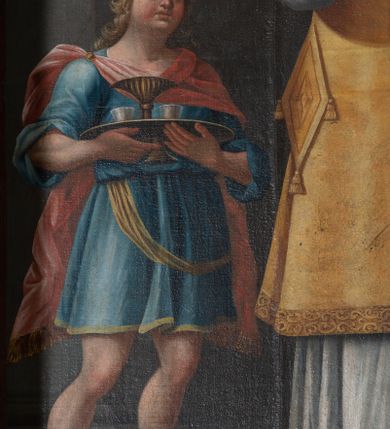 Zdjęcie nr 5: Obraz w formie stojącego prostokąta. W centrum przedstawienie św. Mikołaja z Jezusem i Marią unoszących się na obłokach w górnej części dzieła. Święty ukazany w całej postaci, frontalnie, lewą ręką podtrzymuje księgę z trzema kulami, prawą unosi z dłonią w geście błogosławieństwa. Twarz ma kwadratową z wysokim czołem, o starczych rysach, dużych oczach, prostym nosie i pełnych, rozchylonych ustach, okoloną siwą, kręcona brodą oraz siwymi, kręconymi włosami, sięgającymi ramion. Święty ubrany jest w strój biskupa wschodniego: biały sticharion, żółty sakkos z palicą przy boku oraz omoforion, na stopach ma buty. Po lewej stronie świętego znajduje się szaflik z trójką dzieci. Po jego prawej stronie postać młodzieńca, o pełnej, rumianej twarzy, okolonej jasnymi, kręconymi włosami, ubranego w niebieską tunikę sięgającą kolan oraz jasnoczerwony płaszcz zapięty na prawym ramieniu. Chłopiec trzyma tacę z karafką i dwoma kubkami. Postacie ukazane we wnętrzu. W górnej części obrazu centrycznie rozchodzące się, rozświetlone obłoki. W prawym górnym rogu siedząca na obłoku postać Chrystusa, skierowanego w trzech czwartych w lewo, który w lewej ręce trzyma księgę, a w prawej, opartej na globie, berło. Ubrany jest w czerwoną tunikę i biały płaszcz. Księgę podaje mu putto. W lewym górnym rogu siedząca na obłoku postać Marii, zwróconej w trzech czwartych w prawo, w obu wyciągniętych w przód dłoniach trzyma omoforion. Ubrana jest w jasnoróżową tunikę, przepasaną w talii, niebieski płaszcz i zielony welon. 
