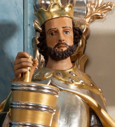 Zdjęcie nr 2: Rzeźba drążona, ustawiona na cokole. Postać przedstawiona frontalnie, w kontrapoście. W prawej, uniesionej w górę ręce trzyma cebrzyk na wodę, w lewej chorągiew z krzyżem łacińskim. Twarz ma pociągłą, okoloną krótką brodą, o szeroko otwartych oczach i wysokim czole. Włosy ma kręcone, zaczesane do tyłu, na głowie mitrę książęcą. Święty ubrany jest w tunikę sięgającą kolan, puklerz, nagolenniki oraz spięty pod szyją płaszcz z gronostajem. Polichromia naturalistyczna w odsłoniętych partiach ciała, elementy zbroi srebrzone, tkanina i atrybuty złocone i srebrzone. 