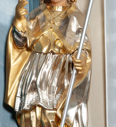 Zdjęcie nr 4: Rzeźba drążona, na cokole. Święty zwrócony frontalnie, w kontrapoście, o esowato wygiętej sylwetce, z głową przechyloną na prawe ramię. Prawą rękę unosi w geście błogosławieństwa, w lewej trzyma pastorał. Twarz ma pociągłą, oczy niewielkie, wydatny nos. Włosy długie, kręcone, opadające na ramiona. Jest ubrany w złoconą albę, srebrzoną komżę z koronką przy brzegu, złocony mucet z guzikami oraz srebrzony płaszcz zapięty na piersi, ze złoconą lamówką i podbiciem; na głowie ma złoconą infułę, na dłoniach rękawiczki. Polichromia naturalistyczna w odsłoniętych partiach ciała, strój i atrybuty złocone i srebrzone.