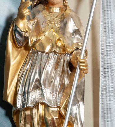 Zdjęcie nr 3: Rzeźba drążona, na cokole. Święty zwrócony frontalnie, w kontrapoście, o esowato wygiętej sylwetce, z głową przechyloną na prawe ramię. Prawą rękę unosi w geście błogosławieństwa, w lewej trzyma pastorał. Twarz ma pociągłą, oczy niewielkie, wydatny nos. Włosy długie, kręcone, opadające na ramiona. Jest ubrany w złoconą albę, srebrzoną komżę z koronką przy brzegu, złocony mucet z guzikami oraz srebrzony płaszcz zapięty na piersi, ze złoconą lamówką i podbiciem; na głowie ma złoconą infułę, na dłoniach rękawiczki. Polichromia naturalistyczna w odsłoniętych partiach ciała, strój i atrybuty złocone i srebrzone.