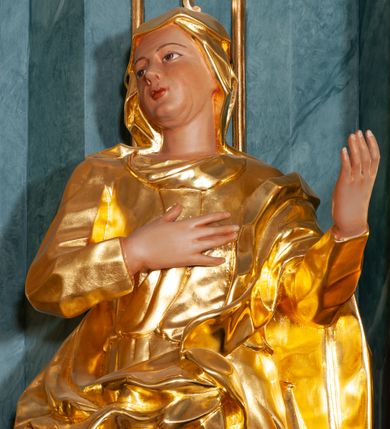 Zdjęcie nr 4: Rzeźba ścięta z tyłu, drążona, ustawiona na rzeźbionym cokole. Święta zwrócona frontalnie, w kontrapoście, z prawym kolanem ugiętym, głową skierowaną w prawą stronę, prawą ręką na piersi i lewą uniesioną. Twarz ma pełną, o delikatnych rysach, oczy i usta niewielkie. Ubrana jest w gęsto drapowaną suknię, przepasaną w talii oraz przerzucony przez lewe ramię płaszcz otaczający postać i opadający na prawą nogę. Na głowie ma ściśle przylegający welon z podwiką. Polichromia naturalistyczna w odsłoniętych partiach ciała, szaty złocone.