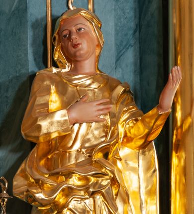 Zdjęcie nr 1: Rzeźba ścięta z tyłu, drążona, ustawiona na rzeźbionym cokole. Święta zwrócona frontalnie, w kontrapoście, z prawym kolanem ugiętym, głową skierowaną w prawą stronę, prawą ręką na piersi i lewą uniesioną. Twarz ma pełną, o delikatnych rysach, oczy i usta niewielkie. Ubrana jest w gęsto drapowaną suknię, przepasaną w talii oraz przerzucony przez lewe ramię płaszcz otaczający postać i opadający na prawą nogę. Na głowie ma ściśle przylegający welon z podwiką. Polichromia naturalistyczna w odsłoniętych partiach ciała, szaty złocone.