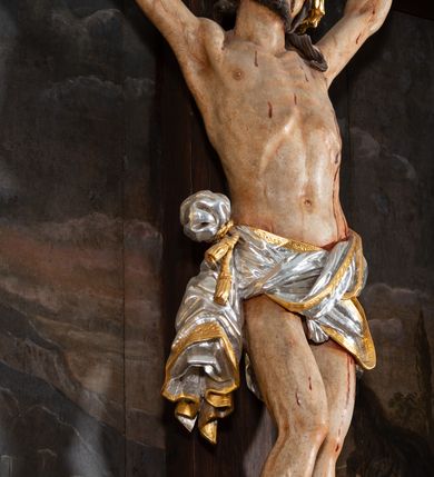 Zdjęcie nr 4: Pole główne ołtarza wypełnia figura Chrystusa Ukrzyżowanego na tle obrazu. Rzeźba pełna przedstawia żywego jeszcze Zbawiciela. Ciało oddano w dużym zwisie, o układzie ramion zbliżonym do litery „V” i esowato wygiętej sylwetce. Jezus ma nogi ugięte w kolanach, stopy przybite dwoma gwoździami, prawą nad lewą. Ciało szczupłe o wyraźnie podkreślonej muskulaturze i pracy mięśni, z zaznaczonymi śladami męki na lewym boku i w miejscach przebicia gwoździami. Głowa w grubej koronie cierniowej, przechylona na lewe ramię, uniesiona, ze wzrokiem skierowanym do góry. Twarz szczupła, okolona krótką brodą, nos długi, wąski, usta rozchylone. Włosy kręcone w pukle opadają na lewe ramię i plecy. Perizonium krótkie, utworzone ze skręconej, drapowanej i skrzyżowanej tkaniny, ze złoconą lamówką; przewiązane na prawym boku sznurem z chwostami, z obfitym, gęsto drapowanym zwisem sięgającym kolan. Polichromia naturalistyczna w partiach ciała; perizonium srebrzone i złocone, korona cierniowa i sznur złocone. W górnej części pionowej belki krzyża titulus w formie zwoju z napisem „IN/RI”. W tle, po prawej stronie krzyża postać klęczącej Marii Magdaleny, zwróconej w trzech czwartych w stronę Chrytsusa. Jej lewa ręka spoczywa na piersi, prawa ujmuje belkę krzyża. Ma pełną, młodzieńczą twarz, włosy długie, opadające na ramiona i plecy z wplecionymi sznurami pereł. Ubrana jest w białą suknię przewiązaną w talii oraz niebieski płaszcz połamany w grube fałdy na rękawach. U jej nóg puszka na wonności. W lewej dolnej części obrazu przedstawienie Jerozolimy wśród gór. Obraz w połowie przecina jaśniejsza linia horyzontu, powyżej widoczne ciemne niebo z kłębiastymi chmurami. Kolorystyka obrazu ciemna, kontrastująca z figurą Ukrzyżowanego. 