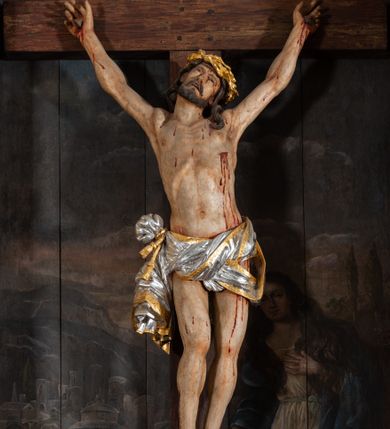 Zdjęcie nr 2: Pole główne ołtarza wypełnia figura Chrystusa Ukrzyżowanego na tle obrazu. Rzeźba pełna przedstawia żywego jeszcze Zbawiciela. Ciało oddano w dużym zwisie, o układzie ramion zbliżonym do litery „V” i esowato wygiętej sylwetce. Jezus ma nogi ugięte w kolanach, stopy przybite dwoma gwoździami, prawą nad lewą. Ciało szczupłe o wyraźnie podkreślonej muskulaturze i pracy mięśni, z zaznaczonymi śladami męki na lewym boku i w miejscach przebicia gwoździami. Głowa w grubej koronie cierniowej, przechylona na lewe ramię, uniesiona, ze wzrokiem skierowanym do góry. Twarz szczupła, okolona krótką brodą, nos długi, wąski, usta rozchylone. Włosy kręcone w pukle opadają na lewe ramię i plecy. Perizonium krótkie, utworzone ze skręconej, drapowanej i skrzyżowanej tkaniny, ze złoconą lamówką; przewiązane na prawym boku sznurem z chwostami, z obfitym, gęsto drapowanym zwisem sięgającym kolan. Polichromia naturalistyczna w partiach ciała; perizonium srebrzone i złocone, korona cierniowa i sznur złocone. W górnej części pionowej belki krzyża titulus w formie zwoju z napisem „IN/RI”. W tle, po prawej stronie krzyża postać klęczącej Marii Magdaleny, zwróconej w trzech czwartych w stronę Chrytsusa. Jej lewa ręka spoczywa na piersi, prawa ujmuje belkę krzyża. Ma pełną, młodzieńczą twarz, włosy długie, opadające na ramiona i plecy z wplecionymi sznurami pereł. Ubrana jest w białą suknię przewiązaną w talii oraz niebieski płaszcz połamany w grube fałdy na rękawach. U jej nóg puszka na wonności. W lewej dolnej części obrazu przedstawienie Jerozolimy wśród gór. Obraz w połowie przecina jaśniejsza linia horyzontu, powyżej widoczne ciemne niebo z kłębiastymi chmurami. Kolorystyka obrazu ciemna, kontrastująca z figurą Ukrzyżowanego. 