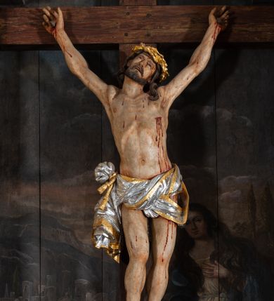 Zdjęcie nr 1: Pole główne ołtarza wypełnia figura Chrystusa Ukrzyżowanego na tle obrazu. Rzeźba pełna przedstawia żywego jeszcze Zbawiciela. Ciało oddano w dużym zwisie, o układzie ramion zbliżonym do litery „V” i esowato wygiętej sylwetce. Jezus ma nogi ugięte w kolanach, stopy przybite dwoma gwoździami, prawą nad lewą. Ciało szczupłe o wyraźnie podkreślonej muskulaturze i pracy mięśni, z zaznaczonymi śladami męki na lewym boku i w miejscach przebicia gwoździami. Głowa w grubej koronie cierniowej, przechylona na lewe ramię, uniesiona, ze wzrokiem skierowanym do góry. Twarz szczupła, okolona krótką brodą, nos długi, wąski, usta rozchylone. Włosy kręcone w pukle opadają na lewe ramię i plecy. Perizonium krótkie, utworzone ze skręconej, drapowanej i skrzyżowanej tkaniny, ze złoconą lamówką; przewiązane na prawym boku sznurem z chwostami, z obfitym, gęsto drapowanym zwisem sięgającym kolan. Polichromia naturalistyczna w partiach ciała; perizonium srebrzone i złocone, korona cierniowa i sznur złocone. W górnej części pionowej belki krzyża titulus w formie zwoju z napisem „IN/RI”. W tle, po prawej stronie krzyża postać klęczącej Marii Magdaleny, zwróconej w trzech czwartych w stronę Chrytsusa. Jej lewa ręka spoczywa na piersi, prawa ujmuje belkę krzyża. Ma pełną, młodzieńczą twarz, włosy długie, opadające na ramiona i plecy z wplecionymi sznurami pereł. Ubrana jest w białą suknię przewiązaną w talii oraz niebieski płaszcz połamany w grube fałdy na rękawach. U jej nóg puszka na wonności. W lewej dolnej części obrazu przedstawienie Jerozolimy wśród gór. Obraz w połowie przecina jaśniejsza linia horyzontu, powyżej widoczne ciemne niebo z kłębiastymi chmurami. Kolorystyka obrazu ciemna, kontrastująca z figurą Ukrzyżowanego. 