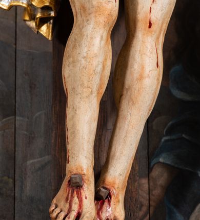 Zdjęcie nr 17: Pole główne ołtarza wypełnia figura Chrystusa Ukrzyżowanego na tle obrazu. Rzeźba pełna przedstawia żywego jeszcze Zbawiciela. Ciało oddano w dużym zwisie, o układzie ramion zbliżonym do litery „V” i esowato wygiętej sylwetce. Jezus ma nogi ugięte w kolanach, stopy przybite dwoma gwoździami, prawą nad lewą. Ciało szczupłe o wyraźnie podkreślonej muskulaturze i pracy mięśni, z zaznaczonymi śladami męki na lewym boku i w miejscach przebicia gwoździami. Głowa w grubej koronie cierniowej, przechylona na lewe ramię, uniesiona, ze wzrokiem skierowanym do góry. Twarz szczupła, okolona krótką brodą, nos długi, wąski, usta rozchylone. Włosy kręcone w pukle opadają na lewe ramię i plecy. Perizonium krótkie, utworzone ze skręconej, drapowanej i skrzyżowanej tkaniny, ze złoconą lamówką; przewiązane na prawym boku sznurem z chwostami, z obfitym, gęsto drapowanym zwisem sięgającym kolan. Polichromia naturalistyczna w partiach ciała; perizonium srebrzone i złocone, korona cierniowa i sznur złocone. W górnej części pionowej belki krzyża titulus w formie zwoju z napisem „IN/RI”. W tle, po prawej stronie krzyża postać klęczącej Marii Magdaleny, zwróconej w trzech czwartych w stronę Chrytsusa. Jej lewa ręka spoczywa na piersi, prawa ujmuje belkę krzyża. Ma pełną, młodzieńczą twarz, włosy długie, opadające na ramiona i plecy z wplecionymi sznurami pereł. Ubrana jest w białą suknię przewiązaną w talii oraz niebieski płaszcz połamany w grube fałdy na rękawach. U jej nóg puszka na wonności. W lewej dolnej części obrazu przedstawienie Jerozolimy wśród gór. Obraz w połowie przecina jaśniejsza linia horyzontu, powyżej widoczne ciemne niebo z kłębiastymi chmurami. Kolorystyka obrazu ciemna, kontrastująca z figurą Ukrzyżowanego. 