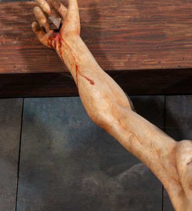 Zdjęcie nr 19: Pole główne ołtarza wypełnia figura Chrystusa Ukrzyżowanego na tle obrazu. Rzeźba pełna przedstawia żywego jeszcze Zbawiciela. Ciało oddano w dużym zwisie, o układzie ramion zbliżonym do litery „V” i esowato wygiętej sylwetce. Jezus ma nogi ugięte w kolanach, stopy przybite dwoma gwoździami, prawą nad lewą. Ciało szczupłe o wyraźnie podkreślonej muskulaturze i pracy mięśni, z zaznaczonymi śladami męki na lewym boku i w miejscach przebicia gwoździami. Głowa w grubej koronie cierniowej, przechylona na lewe ramię, uniesiona, ze wzrokiem skierowanym do góry. Twarz szczupła, okolona krótką brodą, nos długi, wąski, usta rozchylone. Włosy kręcone w pukle opadają na lewe ramię i plecy. Perizonium krótkie, utworzone ze skręconej, drapowanej i skrzyżowanej tkaniny, ze złoconą lamówką; przewiązane na prawym boku sznurem z chwostami, z obfitym, gęsto drapowanym zwisem sięgającym kolan. Polichromia naturalistyczna w partiach ciała; perizonium srebrzone i złocone, korona cierniowa i sznur złocone. W górnej części pionowej belki krzyża titulus w formie zwoju z napisem „IN/RI”. W tle, po prawej stronie krzyża postać klęczącej Marii Magdaleny, zwróconej w trzech czwartych w stronę Chrytsusa. Jej lewa ręka spoczywa na piersi, prawa ujmuje belkę krzyża. Ma pełną, młodzieńczą twarz, włosy długie, opadające na ramiona i plecy z wplecionymi sznurami pereł. Ubrana jest w białą suknię przewiązaną w talii oraz niebieski płaszcz połamany w grube fałdy na rękawach. U jej nóg puszka na wonności. W lewej dolnej części obrazu przedstawienie Jerozolimy wśród gór. Obraz w połowie przecina jaśniejsza linia horyzontu, powyżej widoczne ciemne niebo z kłębiastymi chmurami. Kolorystyka obrazu ciemna, kontrastująca z figurą Ukrzyżowanego. 