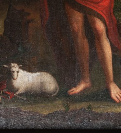 Zdjęcie nr 6: Obraz w kształcie stojącego prostokąta w profilowanej, złoconej i srebrzonej ramie z przedstawieniem św. Jana Chrzciciela. Święty stoi w centrum kompozycji w lekkim kontrapoście, skręcony delikatnie w prawo, z głową obróconą na lewe ramię. Prawą rękę unosi do boku, w lewej trzyma długie drzewce zakończone krzyżem z przewiązaną banderolą z napisem „ECCE AGNUS DEI”. Ma szczupłą, owalną twarz z wysokim czołem, wąskim nosem i dużymi, ciemnymi oczami. Nosi wąsy i krótką brodę, a długie włosy spływają mu na plecy. Święty ma narzucony czerwony, podbity brązem płaszcz przewiązany na lewym ramieniu szarfą, przerzucony przez prawe przedramię i otaczający biodra. U jego stóp, po lewej stronie kompozycji, na księdze w czerwonej oprawie leży niewielki baranek. Z prawej strony u dołu widać wznoszącą wzrok na świętego rodzinę złożoną ze starszego mężczyzny w niebieskiej sukni i żółtym płaszczu, kobiety w jasnych szatach i dziecka. Święty Jan został ukazany na tle ciemnego lasu lub bloku skalnego i skłębionego, szarego obłoku, ponad którym unosi się główka anielska. Przy prawej krawędzi widoczny fragment szerokiego krajobrazu stanowiącego brzeg rzeki lub morza. 