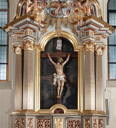 Zdjęcie nr 6: Nastawa ołtarzowa jednoosiowa, jednokondygnacyjna ze zwieńczeniem, na podwójnym cokole. Mensa ołtarzowa drewniana, prostopadłościenna. Antepedium w formie leżącego prostokąta w profilowanej ramie. Pole dekorowane rzeźbionym akantem o układzie symetrycznym względem osi środkowej, z elementami muszli oraz parą puttów po dwóch stronach centralnie ustawionej łodygi z kwiatem. Tabernakulum w formie prostopadłościanu zamkniętego gzymsem. Drzwiczki w kształcie stojącego prostokąta zamkniętego łukiem nadwieszonym w profilowanej ramie z płaskorzeźbionym przedstawieniem zmartwychwstałego Chrystusa; ujęte płyciną, dekorowaną w przyłuczach polami z akantem. Chrystus został ukazany w całej postaci, lewą ręka przytrzymując krzyż, prawą wskazuje ranę w boku. Przy jego prawej nodze stoi kielich. Pierwsza kondygnacja nastawy ujęta dwiema parami kolumn o kapitelach kompozytowych i kanelowanych trzonach o kwadratowym przekroju, ustawionych przed pilastrami; wewnętrzna para ustawiona skośnie względem lica ołtarza. Podpory dźwigają pełne belkowanie wyłamane na ich osi, przerwane nad polem środkowym; wewnętrzna para podtrzymuje imposty oraz przerwany, esowaty przyczółek z siedzącymi przed nim, na gzymsie, figurami aniołów w długich sukniach. Pole środkowe kondygnacji w formie stojącego prostokąta zamkniętego łukiem półkolistym nadwieszonym z wnęką z figurą Chrystusa Ukrzyżowanego na malowanym tle z Jerozolimą i postacią św. Marii Magdaleny. Zwieńczenie w formie bardzo rozbudowanej glorii promienistej, o naprzemiennie długich i krótkich wiązkach promieni; z płaskorzeźbionym mandylionem podtrzymywanym u spodu i po bokach przez trzy putta. Chustę św. Weroniki od góry i od dołu ujmują skłębione obłoki, między którymi widoczne główki anielskie. 
Oba cokoły dekorowane płycinami: w partii dolnego cokołu wypełnionymi ciemnoróżową marmoryzacją, w partii górnego ornamentem akantowym, mniejsze płyciny w partii fryzu. Struktura polichromowana na kolor jasnoszary, pola płycin i profilowania czerwone; kolumny, gloria, ornamentyka i profilowania złocone; chusta i obłoki srebrzone.
