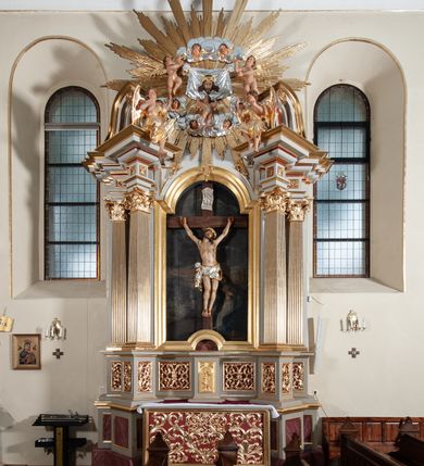 Zdjęcie nr 2: Nastawa ołtarzowa jednoosiowa, jednokondygnacyjna ze zwieńczeniem, na podwójnym cokole. Mensa ołtarzowa drewniana, prostopadłościenna. Antepedium w formie leżącego prostokąta w profilowanej ramie. Pole dekorowane rzeźbionym akantem o układzie symetrycznym względem osi środkowej, z elementami muszli oraz parą puttów po dwóch stronach centralnie ustawionej łodygi z kwiatem. Tabernakulum w formie prostopadłościanu zamkniętego gzymsem. Drzwiczki w kształcie stojącego prostokąta zamkniętego łukiem nadwieszonym w profilowanej ramie z płaskorzeźbionym przedstawieniem zmartwychwstałego Chrystusa; ujęte płyciną, dekorowaną w przyłuczach polami z akantem. Chrystus został ukazany w całej postaci, lewą ręka przytrzymując krzyż, prawą wskazuje ranę w boku. Przy jego prawej nodze stoi kielich. Pierwsza kondygnacja nastawy ujęta dwiema parami kolumn o kapitelach kompozytowych i kanelowanych trzonach o kwadratowym przekroju, ustawionych przed pilastrami; wewnętrzna para ustawiona skośnie względem lica ołtarza. Podpory dźwigają pełne belkowanie wyłamane na ich osi, przerwane nad polem środkowym; wewnętrzna para podtrzymuje imposty oraz przerwany, esowaty przyczółek z siedzącymi przed nim, na gzymsie, figurami aniołów w długich sukniach. Pole środkowe kondygnacji w formie stojącego prostokąta zamkniętego łukiem półkolistym nadwieszonym z wnęką z figurą Chrystusa Ukrzyżowanego na malowanym tle z Jerozolimą i postacią św. Marii Magdaleny. Zwieńczenie w formie bardzo rozbudowanej glorii promienistej, o naprzemiennie długich i krótkich wiązkach promieni; z płaskorzeźbionym mandylionem podtrzymywanym u spodu i po bokach przez trzy putta. Chustę św. Weroniki od góry i od dołu ujmują skłębione obłoki, między którymi widoczne główki anielskie. 
Oba cokoły dekorowane płycinami: w partii dolnego cokołu wypełnionymi ciemnoróżową marmoryzacją, w partii górnego ornamentem akantowym, mniejsze płyciny w partii fryzu. Struktura polichromowana na kolor jasnoszary, pola płycin i profilowania czerwone; kolumny, gloria, ornamentyka i profilowania złocone; chusta i obłoki srebrzone.
