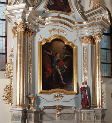 Zdjęcie nr 2: Nastawa ołtarzowa jednoosiowa, jednokondygnacyjna ze zwieńczeniem, na podwójnym cokole. Mensa drewniana, sarkofagowa. W polu antepedium stylizowane elementy rocaille’owe ujęte ornamentem roślinnym. Kondygnacja nastawy flankowana pilastrami oraz stojącą przed nimi parą kolumn o kapitelach kompozytowych. Cokoły kolumn profilowane, ustawione skośnie względem lica. Podpory dźwigają pełne belkowanie o wklęsłej linii, wyłamane na ich osiach, połączone nad polem środkowym gzymsem wygiętym w łuk oraz fragmenty przerwanego przyczółka z klęczącą parą adorujących aniołów. W polu środkowym obraz z przedstawieniem św. Michała Archanioła ujęty profilowaną ramą w formie stojącego prostokąta z dolną krawędzią wyniesioną w łuk i zamkniętego łukiem nadwieszonym z uskokiem. Na cokołach, obok kolumn, po lewej stronie wazon z kwiatami, po prawej święta niewiasta (św. Anna?). Kondygnacja ujęta ażurowymi uszami utworzonymi z rocaille’ów, kratki regencyjnej oraz rozwiniętych kwiatów. Zwieńczenie w formie zbliżonej do stojącego prostokąta o wklęsłych bokach zwężających się ku górze z uszakami, zamknięte falistym gzymsem. W polu obraz z przedstawieniem św. Hieronima w profilowanej ramie w formie stojącego prostokąta o wklęsłych bokach i dolnych narożach rozszerzającego się ku dołowi, zamkniętego łukiem nadwieszonym z uskokami. Cokoły nastawy dekorowane płycinami o fantazyjnym zarysie oraz w formie leżących prostokątów. Trzony pilastrów zdobione płycinami; wewnętrzna para wypełniona rocaille’em. Pole główne, zwieńczenie oraz uszaki dekorowane elementami rocaille’owymi. Zwieńczenie ujęte roślinnymi festonami. Struktura polichromowana na biało; cokoły, ołtarz i predella marmoryzowane w kolorze beżowym; kolumny, ornamentyka i profile złocone i srebrzone.