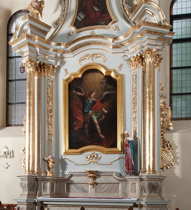 Zdjęcie nr 4: Nastawa ołtarzowa jednoosiowa, jednokondygnacyjna ze zwieńczeniem, na podwójnym cokole. Mensa drewniana, sarkofagowa. W polu antepedium stylizowane elementy rocaille’owe ujęte ornamentem roślinnym. Kondygnacja nastawy flankowana pilastrami oraz stojącą przed nimi parą kolumn o kapitelach kompozytowych. Cokoły kolumn profilowane, ustawione skośnie względem lica. Podpory dźwigają pełne belkowanie o wklęsłej linii, wyłamane na ich osiach, połączone nad polem środkowym gzymsem wygiętym w łuk oraz fragmenty przerwanego przyczółka z klęczącą parą adorujących aniołów. W polu środkowym obraz z przedstawieniem św. Michała Archanioła ujęty profilowaną ramą w formie stojącego prostokąta z dolną krawędzią wyniesioną w łuk i zamkniętego łukiem nadwieszonym z uskokiem. Na cokołach, obok kolumn, po lewej stronie wazon z kwiatami, po prawej święta niewiasta (św. Anna?). Kondygnacja ujęta ażurowymi uszami utworzonymi z rocaille’ów, kratki regencyjnej oraz rozwiniętych kwiatów. Zwieńczenie w formie zbliżonej do stojącego prostokąta o wklęsłych bokach zwężających się ku górze z uszakami, zamknięte falistym gzymsem. W polu obraz z przedstawieniem św. Hieronima w profilowanej ramie w formie stojącego prostokąta o wklęsłych bokach i dolnych narożach rozszerzającego się ku dołowi, zamkniętego łukiem nadwieszonym z uskokami. Cokoły nastawy dekorowane płycinami o fantazyjnym zarysie oraz w formie leżących prostokątów. Trzony pilastrów zdobione płycinami; wewnętrzna para wypełniona rocaille’em. Pole główne, zwieńczenie oraz uszaki dekorowane elementami rocaille’owymi. Zwieńczenie ujęte roślinnymi festonami. Struktura polichromowana na biało; cokoły, ołtarz i predella marmoryzowane w kolorze beżowym; kolumny, ornamentyka i profile złocone i srebrzone.