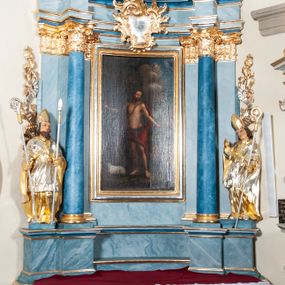 Zdjęcie nr 1: Nastawa ołtarzowa jednoosiowa, jednokondygnacyjna ze zwieńczeniem, na podwójnym cokole. Mensa drewniana, prostopadłościenna. Antepedium w formie leżącego prostokąta ujęte profilowaną ramą. W polu płaskorzeźbiona półpostać św. Augustyna ujętego u spodu płatkami kwiatu, flankowana banderolami. W prawej, uniesionej ręce trzyma księgę, lewą, ugiętą przytrzymuje pastorał, dłonią przyciska do piersi gorejące serce. Święty ukazany został jako starzec. Twarz ma pociągłą, okoloną krótką brodą, włosy sięgające szyi. Ubrany jest w niebieską tunikę i przerzucony przez ramiona płaszcz ze złoconą lamówką. Pole wypełnione jest płaskorzeźbionymi łodygami z kwiatami. Kondygnacja nastawy o wklęsłym licu, ujęta parą zwielokrotnionych pilastrów oraz stojącą przed nimi parą kolumn o kapitelach kompozytowych. Podpory dźwigają pełne belkowanie o silnie wysuniętym gzymsie, wyłamane na ich osi oraz przerwany przyczółek na linii kolumn. Po zewnętrznej stronie kolumn figury św. Wojciecha po lewej i św. Stanisława po prawej. W polu środkowym nisza w formie stojącego prostokąta otoczona profilowaną ramą; wewnątrz mniejszy obraz z przedstawieniem św. Jana Chrzciciela w profilowanym obramieniu w kształcie stojącego prostokąta. Zwieńczenie w kształcie stojącego prostokąta ujętego spływami wolutowymi, zamknięte gzymsem utworzonym ze zwróconych do siebie wolut; zakończone glorią promienistą z okrągłym polem z napisem „IHS” w otoczeniu obłoków. W polu zwieńczenia obraz z przedstawieniem św. Grzegorza w profilowanej ramie w formie stojącego prostokąta o wklęsłych bokach i narożach, zamkniętej łukiem nadwieszonym. Kondygnacja ujęta ażurowymi uszami utworzonymi z motywów roślinnych i karbowanej wstęgi. W partii belkowania nad polem środkowym rocaille&#039;owy kartusz. Nad obrazem w zwieńczeniu muszla i kampanule; woluty dekorowane festonami. Struktura polichromowana na kolor jasnoniebieski; trzony kolumn, antepedium i profile na niebiesko; ornamentyka i profile złocone.