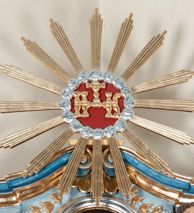 Zdjęcie nr 7: Nastawa ołtarzowa jednoosiowa, jednokondygnacyjna ze zwieńczeniem, na podwójnym cokole. Mensa drewniana, prostopadłościenna. Antepedium w formie leżącego prostokąta ujęte profilowaną ramą. W polu płaskorzeźbiona półpostać św. Augustyna ujętego u spodu płatkami kwiatu, flankowana banderolami. W prawej, uniesionej ręce trzyma księgę, lewą, ugiętą przytrzymuje pastorał, dłonią przyciska do piersi gorejące serce. Święty ukazany został jako starzec. Twarz ma pociągłą, okoloną krótką brodą, włosy sięgające szyi. Ubrany jest w niebieską tunikę i przerzucony przez ramiona płaszcz ze złoconą lamówką. Pole wypełnione jest płaskorzeźbionymi łodygami z kwiatami. Kondygnacja nastawy o wklęsłym licu, ujęta parą zwielokrotnionych pilastrów oraz stojącą przed nimi parą kolumn o kapitelach kompozytowych. Podpory dźwigają pełne belkowanie o silnie wysuniętym gzymsie, wyłamane na ich osi oraz przerwany przyczółek na linii kolumn. Po zewnętrznej stronie kolumn figury św. Wojciecha po lewej i św. Stanisława po prawej. W polu środkowym nisza w formie stojącego prostokąta otoczona profilowaną ramą; wewnątrz mniejszy obraz z przedstawieniem św. Jana Chrzciciela w profilowanym obramieniu w kształcie stojącego prostokąta. Zwieńczenie w kształcie stojącego prostokąta ujętego spływami wolutowymi, zamknięte gzymsem utworzonym ze zwróconych do siebie wolut; zakończone glorią promienistą z okrągłym polem z napisem „IHS” w otoczeniu obłoków. W polu zwieńczenia obraz z przedstawieniem św. Grzegorza w profilowanej ramie w formie stojącego prostokąta o wklęsłych bokach i narożach, zamkniętej łukiem nadwieszonym. Kondygnacja ujęta ażurowymi uszami utworzonymi z motywów roślinnych i karbowanej wstęgi. W partii belkowania nad polem środkowym rocaille'owy kartusz. Nad obrazem w zwieńczeniu muszla i kampanule; woluty dekorowane festonami. Struktura polichromowana na kolor jasnoniebieski; trzony kolumn, antepedium i profile na niebiesko; ornamentyka i profile złocone.