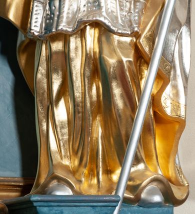 Zdjęcie nr 18: Nastawa ołtarzowa jednoosiowa, jednokondygnacyjna ze zwieńczeniem, na podwójnym cokole. Mensa drewniana, prostopadłościenna. Antepedium w formie leżącego prostokąta ujęte profilowaną ramą. W polu płaskorzeźbiona półpostać św. Augustyna ujętego u spodu płatkami kwiatu, flankowana banderolami. W prawej, uniesionej ręce trzyma księgę, lewą, ugiętą przytrzymuje pastorał, dłonią przyciska do piersi gorejące serce. Święty ukazany został jako starzec. Twarz ma pociągłą, okoloną krótką brodą, włosy sięgające szyi. Ubrany jest w niebieską tunikę i przerzucony przez ramiona płaszcz ze złoconą lamówką. Pole wypełnione jest płaskorzeźbionymi łodygami z kwiatami. Kondygnacja nastawy o wklęsłym licu, ujęta parą zwielokrotnionych pilastrów oraz stojącą przed nimi parą kolumn o kapitelach kompozytowych. Podpory dźwigają pełne belkowanie o silnie wysuniętym gzymsie, wyłamane na ich osi oraz przerwany przyczółek na linii kolumn. Po zewnętrznej stronie kolumn figury św. Wojciecha po lewej i św. Stanisława po prawej. W polu środkowym nisza w formie stojącego prostokąta otoczona profilowaną ramą; wewnątrz mniejszy obraz z przedstawieniem św. Jana Chrzciciela w profilowanym obramieniu w kształcie stojącego prostokąta. Zwieńczenie w kształcie stojącego prostokąta ujętego spływami wolutowymi, zamknięte gzymsem utworzonym ze zwróconych do siebie wolut; zakończone glorią promienistą z okrągłym polem z napisem „IHS” w otoczeniu obłoków. W polu zwieńczenia obraz z przedstawieniem św. Grzegorza w profilowanej ramie w formie stojącego prostokąta o wklęsłych bokach i narożach, zamkniętej łukiem nadwieszonym. Kondygnacja ujęta ażurowymi uszami utworzonymi z motywów roślinnych i karbowanej wstęgi. W partii belkowania nad polem środkowym rocaille'owy kartusz. Nad obrazem w zwieńczeniu muszla i kampanule; woluty dekorowane festonami. Struktura polichromowana na kolor jasnoniebieski; trzony kolumn, antepedium i profile na niebiesko; ornamentyka i profile złocone.