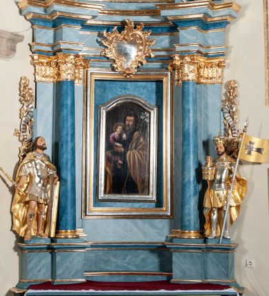 Zdjęcie nr 1: Nastawa ołtarzowa jednoosiowa, jednokondygnacyjna ze zwieńczeniem, na podwójnym cokole. Mensa drewniana, prostopadłościenna. Antepedium w formie leżącego prostokąta ujęte profilowaną ramą. W polu płaskorzeźbiona półpostać św. Hieronima, ujętego płatkami kwiatu na długiej, wygiętej łodydze, flankowana parą banderol. Prawą, ugiętą ręką podtrzymuje podwójny krzyż, w dłoni zaś kamień; lewą wyciągniętą w bok trzyma otwartą księgę. Święty ukazany został jako starzec. Twarz ma pociągłą, o wysokim czole, okoloną długą brodą; włosy po bokach głowy. Tors odsłonięty, postać przewiązana wokół gęsto drapowanym płaszczem. Przy prawym boku lew. Pole wypełnione płaskorzeźbionymi, wijącymi się ukwieconymi łodygami. Kondygnacja nastawy o wklęsłym licu, ujęta parą zwielokrotnionych pilastrów oraz stojącą przed nimi parą kolumn o kapitelach kompozytowych. Podpory dźwigają pełne belkowanie o silnie wysuniętym gzymsie, wyłamane na ich osi oraz przerwany przyczółek na linii kolumn na którym siedzi para puttów. Po zewnętrznej stronie kolumn figury króla Dawida po lewej i św. Floriana po prawej stronie. W polu środkowym nisza w formie stojącego prostokąta ujęta profilowaną ramą; wewnątrz mniejszy obraz z przedstawieniem św. Józefa w profilowanej ramie w kształcie stojącego prostokąta zwieńczonego łukiem wklęsło-wypukłym. Zwieńczenie w postaci stojącego prostokąta o wklęsłych bokach ujętego spływami wolutowymi i zakończone glorią promienistą z płaskorzeźbionym monogramem MARYA w otoczeniu obłoków. W polu obraz z przedstawieniem św. Grzegorza w profilowanej ramie w formie stojącego prostokąta o wklęsłych bokach i narożach, zamkniętej łukiem nadwieszonym. Kondygnacja ujęta ażurowymi uszami utworzonymi z motywów roślinnych i karbowanej wstęgi. W partii belkowania nad polem środkowym rocaille’owy kartusz. Nad obrazem, w zwieńczeniu, muszla i kampanule; woluty dekorowane festonami. Struktura polichromowana na kolor jasnoniebieski; trzony kolumn, antepedium i profile na niebiesko; ornamentyka i profile złocone i srebrzone.