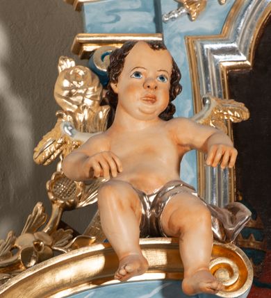 Zdjęcie nr 9: Nastawa ołtarzowa jednoosiowa, jednokondygnacyjna ze zwieńczeniem, na podwójnym cokole. Mensa drewniana, prostopadłościenna. Antepedium w formie leżącego prostokąta ujęte profilowaną ramą. W polu płaskorzeźbiona półpostać św. Hieronima, ujętego płatkami kwiatu na długiej, wygiętej łodydze, flankowana parą banderol. Prawą, ugiętą ręką podtrzymuje podwójny krzyż, w dłoni zaś kamień; lewą wyciągniętą w bok trzyma otwartą księgę. Święty ukazany został jako starzec. Twarz ma pociągłą, o wysokim czole, okoloną długą brodą; włosy po bokach głowy. Tors odsłonięty, postać przewiązana wokół gęsto drapowanym płaszczem. Przy prawym boku lew. Pole wypełnione płaskorzeźbionymi, wijącymi się ukwieconymi łodygami. Kondygnacja nastawy o wklęsłym licu, ujęta parą zwielokrotnionych pilastrów oraz stojącą przed nimi parą kolumn o kapitelach kompozytowych. Podpory dźwigają pełne belkowanie o silnie wysuniętym gzymsie, wyłamane na ich osi oraz przerwany przyczółek na linii kolumn na którym siedzi para puttów. Po zewnętrznej stronie kolumn figury króla Dawida po lewej i św. Floriana po prawej stronie. W polu środkowym nisza w formie stojącego prostokąta ujęta profilowaną ramą; wewnątrz mniejszy obraz z przedstawieniem św. Józefa w profilowanej ramie w kształcie stojącego prostokąta zwieńczonego łukiem wklęsło-wypukłym. Zwieńczenie w postaci stojącego prostokąta o wklęsłych bokach ujętego spływami wolutowymi i zakończone glorią promienistą z płaskorzeźbionym monogramem MARYA w otoczeniu obłoków. W polu obraz z przedstawieniem św. Grzegorza w profilowanej ramie w formie stojącego prostokąta o wklęsłych bokach i narożach, zamkniętej łukiem nadwieszonym. Kondygnacja ujęta ażurowymi uszami utworzonymi z motywów roślinnych i karbowanej wstęgi. W partii belkowania nad polem środkowym rocaille’owy kartusz. Nad obrazem, w zwieńczeniu, muszla i kampanule; woluty dekorowane festonami. Struktura polichromowana na kolor jasnoniebieski; trzony kolumn, antepedium i profile na niebiesko; ornamentyka i profile złocone i srebrzone.