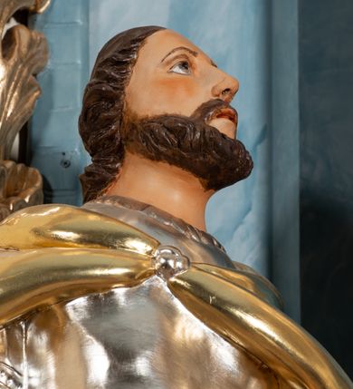 Zdjęcie nr 13: Nastawa ołtarzowa jednoosiowa, jednokondygnacyjna ze zwieńczeniem, na podwójnym cokole. Mensa drewniana, prostopadłościenna. Antepedium w formie leżącego prostokąta ujęte profilowaną ramą. W polu płaskorzeźbiona półpostać św. Hieronima, ujętego płatkami kwiatu na długiej, wygiętej łodydze, flankowana parą banderol. Prawą, ugiętą ręką podtrzymuje podwójny krzyż, w dłoni zaś kamień; lewą wyciągniętą w bok trzyma otwartą księgę. Święty ukazany został jako starzec. Twarz ma pociągłą, o wysokim czole, okoloną długą brodą; włosy po bokach głowy. Tors odsłonięty, postać przewiązana wokół gęsto drapowanym płaszczem. Przy prawym boku lew. Pole wypełnione płaskorzeźbionymi, wijącymi się ukwieconymi łodygami. Kondygnacja nastawy o wklęsłym licu, ujęta parą zwielokrotnionych pilastrów oraz stojącą przed nimi parą kolumn o kapitelach kompozytowych. Podpory dźwigają pełne belkowanie o silnie wysuniętym gzymsie, wyłamane na ich osi oraz przerwany przyczółek na linii kolumn na którym siedzi para puttów. Po zewnętrznej stronie kolumn figury króla Dawida po lewej i św. Floriana po prawej stronie. W polu środkowym nisza w formie stojącego prostokąta ujęta profilowaną ramą; wewnątrz mniejszy obraz z przedstawieniem św. Józefa w profilowanej ramie w kształcie stojącego prostokąta zwieńczonego łukiem wklęsło-wypukłym. Zwieńczenie w postaci stojącego prostokąta o wklęsłych bokach ujętego spływami wolutowymi i zakończone glorią promienistą z płaskorzeźbionym monogramem MARYA w otoczeniu obłoków. W polu obraz z przedstawieniem św. Grzegorza w profilowanej ramie w formie stojącego prostokąta o wklęsłych bokach i narożach, zamkniętej łukiem nadwieszonym. Kondygnacja ujęta ażurowymi uszami utworzonymi z motywów roślinnych i karbowanej wstęgi. W partii belkowania nad polem środkowym rocaille’owy kartusz. Nad obrazem, w zwieńczeniu, muszla i kampanule; woluty dekorowane festonami. Struktura polichromowana na kolor jasnoniebieski; trzony kolumn, antepedium i profile na niebiesko; ornamentyka i profile złocone i srebrzone.