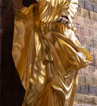 Zdjęcie nr 5: Rzeźba drążona na cokole z przedstawieniem św. Łukasza w całej postaci. Figura w kontrapoście, w skręcie w prawo, z głową zwróconą w lewo; w prawej wyciągniętej w bok ręce trzyma księgę, lewą unosi równolegle. Głowę ma lekko pochyloną; twarz szczupłą z wysokim czołem, o szeroko otwartych, ciemnych oczach, wąskim nosie i rozchylonych ustach. Twarz jest okolona krótkim kręconym zarostem oraz włosami układającymi się w spływające na kark fale. Święty jest ubrany w długą, przylegającą do ciała tunikę oraz płaszcz przewiązany diagonalnie z prawego ramienia przez plecy i wokół lewego biodra, złapany z przodu. Polichromia naturalistyczna w odsłoniętych partiach ciała, szaty złocone, księga brązowo-złota. Z uwagi na swoje aktualne ustawienie na ołtarzu głównym wydrążenie zostało zasłonięte zamalowanym na złoto materiałem.