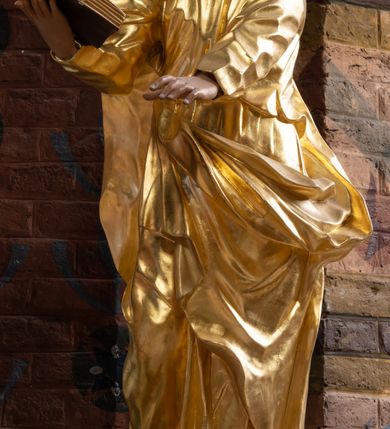 Zdjęcie nr 6: Rzeźba drążona na cokole z przedstawieniem św. Łukasza w całej postaci. Figura w kontrapoście, w skręcie w prawo, z głową zwróconą w lewo; w prawej wyciągniętej w bok ręce trzyma księgę, lewą unosi równolegle. Głowę ma lekko pochyloną; twarz szczupłą z wysokim czołem, o szeroko otwartych, ciemnych oczach, wąskim nosie i rozchylonych ustach. Twarz jest okolona krótkim kręconym zarostem oraz włosami układającymi się w spływające na kark fale. Święty jest ubrany w długą, przylegającą do ciała tunikę oraz płaszcz przewiązany diagonalnie z prawego ramienia przez plecy i wokół lewego biodra, złapany z przodu. Polichromia naturalistyczna w odsłoniętych partiach ciała, szaty złocone, księga brązowo-złota. Z uwagi na swoje aktualne ustawienie na ołtarzu głównym wydrążenie zostało zasłonięte zamalowanym na złoto materiałem.