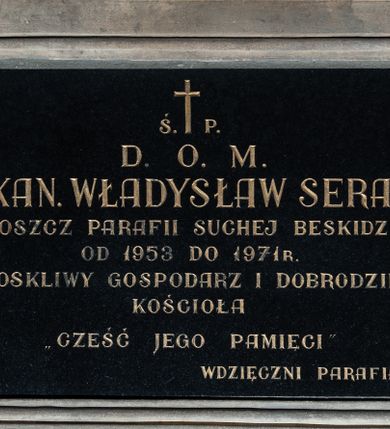 Zdjęcie nr 1: Prostokątna płyta w kształcie leżącego prostokąta, z czarnego marmuru, opatrzona majuskułowym napisem w języku polskim (litery pozłocone): Ś. P. / D. O. M. / KS. KAN. WŁADYSŁAW SERAFIN / PROBOSZCZ PARAFII SUCHEJ BESKIDZKIEJ / OD 1953 DO 1971 R. / TROSKLIWY GOSPODARZ I DOBRODZIEJ / KOŚCIOŁA / CZEŚĆ JEGO PAMIĘCI / WDZIĘCZNI PARAFIANIE. Płyta umieszczona w ramie z piaskowca, profilowanej, prostokątnej, z uszakami w narożach.