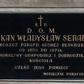 Zdjęcie nr 1: Prostokątna płyta w kształcie leżącego prostokąta, z czarnego marmuru, opatrzona majuskułowym napisem w języku polskim (litery pozłocone): Ś. P. / D. O. M. / KS. KAN. WŁADYSŁAW SERAFIN / PROBOSZCZ PARAFII SUCHEJ BESKIDZKIEJ / OD 1953 DO 1971 R. / TROSKLIWY GOSPODARZ I DOBRODZIEJ / KOŚCIOŁA / CZEŚĆ JEGO PAMIĘCI / WDZIĘCZNI PARAFIANIE. Płyta umieszczona w ramie z piaskowca, profilowanej, prostokątnej, z uszakami w narożach.