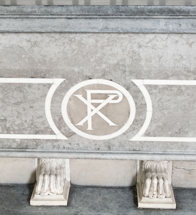 Zdjęcie nr 2: Mensa w typie sarkofagowym ustawiona na czterech lwich łapach. Ściana frontowa jest dekorowana trzema płycinami. Zewnętrzne mają kształt leżących prostokątów z wklęsłą wewnętrzną krawędzią, a środkowa jest okrągła, wypełniona chrystogramem. Mensa w kolorze jasnoszarego kamienia, łapy białe. 