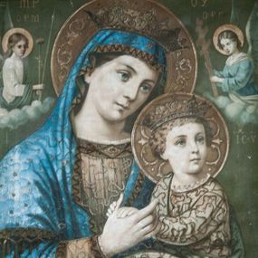 Zdjęcie nr 1: Obraz w kształcie zbliżonym do kwadratu w drewnianej, rzeźbionej w kimation ramie. W centrum ukazana w półpostaci Matka Boska z Dzieciątkiem na lewym ramieniu. Maria ma głowę przechyloną na lewe ramię, w prawej ręce trzyma rękę Dzieciątka. Ma owalną twarz o łagodnym wyrazie, niebieskie oczy, prosty nos i wąskie usta. Jest ubrana w jasnobrązową suknię z ciemniejszą lamówką i niebieski maforion. Dzieciątko siedzi, dłońmi dotyka ręki matki, głowę zwraca w lewo. Jest ubrane w długą, jasną tunikę. Stroje postaci są dekorowane aplikowaną tasiemką, postacie mają na głowach otwarte korony, a wokół głów nimby wypełnione stylizowaną wicią roślinną.  Po obu stronach głowy Marii ukazano anioły trzymające arma Christi. Anioł z lewej jest ubrany w białą suknię i zielony płaszcz, trzyma gąbkę na drzewcu oraz włócznię, a anioł z prawej jest ubrany w niebieską suknię z białymi dodatkami i trzyma krzyż papieski z trzema belkami.  W tle, powyżej aniołów napisy: po lewej stronie „MP” i „ΟΡМ”, a po prawej „ΘΥ” oraz „OΡГ”. Poniżej anioła po prawej stronie „IC-XC”. Tło jednolite, ciemnozielone.