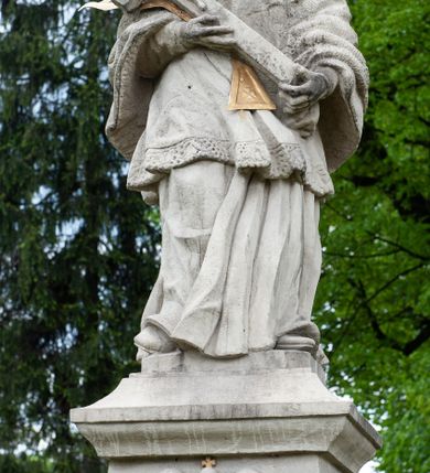 Zdjęcie nr 3: Figura św. Jana Nepomucena na rozbudowanej podstawie. Na trzech stopniach ustawiono sześcian zwężający się ku górze, składający się z postumentu z wolutami w dolnej części ustawionego na cokole i zwieńczonego gzymsem. Na ścianie frontowej na rozpostartej, zwieńczonej mitrą książęcą tkaninie złocona inskrypcja „PROSZĘ / O JEDNO PO/ZDROWIENIE / ZA DUSZE / ZMARŁYCH / A(NNO) D(OMINI) 1759” a poniżej data „R(OKU) 1901” ponad czaszką i piszczelą. Na podstawie, na cokole ustawiono figurę św. Jana Nepomucena w kontrapoście, z prawą nogą ugiętą w kolanie. Obiema rękami przytrzymuje krucyfiks i złotą palmę męczeństwa. Ma podłużną, smutną twarz o wklęsłych policzkach, niewielkich oczach, wąskim nosie i zamkniętych ustach okoloną krótką brodą i krótkimi włosami odwijającymi się do tyłu. Jest ubrany w strój kanonika: ma narzuconą na komżę i sutannę futrzaną almucję, a na głowie biret. Wokół głowy nimb z pięcioma złoconymi gwiazdkami. Na stopniu cokoło napis „ODNOWIŁA RADA GMINNA”. 