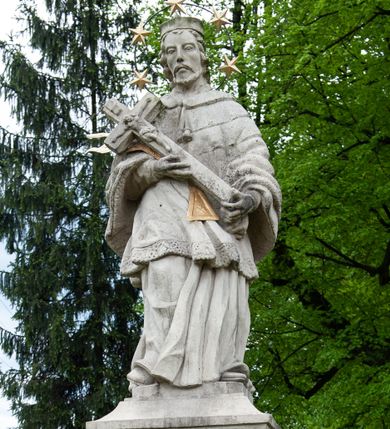 Zdjęcie nr 1: Figura św. Jana Nepomucena na rozbudowanej podstawie. Na trzech stopniach ustawiono sześcian zwężający się ku górze, składający się z postumentu z wolutami w dolnej części ustawionego na cokole i zwieńczonego gzymsem. Na ścianie frontowej na rozpostartej, zwieńczonej mitrą książęcą tkaninie złocona inskrypcja „PROSZĘ / O JEDNO PO/ZDROWIENIE / ZA DUSZE / ZMARŁYCH / A(NNO) D(OMINI) 1759” a poniżej data „R(OKU) 1901” ponad czaszką i piszczelą. Na podstawie, na cokole ustawiono figurę św. Jana Nepomucena w kontrapoście, z prawą nogą ugiętą w kolanie. Obiema rękami przytrzymuje krucyfiks i złotą palmę męczeństwa. Ma podłużną, smutną twarz o wklęsłych policzkach, niewielkich oczach, wąskim nosie i zamkniętych ustach okoloną krótką brodą i krótkimi włosami odwijającymi się do tyłu. Jest ubrany w strój kanonika: ma narzuconą na komżę i sutannę futrzaną almucję, a na głowie biret. Wokół głowy nimb z pięcioma złoconymi gwiazdkami. Na stopniu cokoło napis „ODNOWIŁA RADA GMINNA”. 