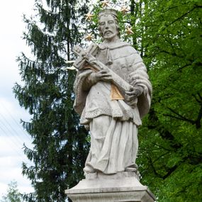 Zdjęcie nr 1: Figura św. Jana Nepomucena na rozbudowanej podstawie. Na trzech stopniach ustawiono sześcian zwężający się ku górze, składający się z postumentu z wolutami w dolnej części ustawionego na cokole i zwieńczonego gzymsem. Na ścianie frontowej na rozpostartej, zwieńczonej mitrą książęcą tkaninie złocona inskrypcja „PROSZĘ / O JEDNO PO/ZDROWIENIE / ZA DUSZE / ZMARŁYCH / A(NNO) D(OMINI) 1759” a poniżej data „R(OKU) 1901” ponad czaszką i piszczelą. Na podstawie, na cokole ustawiono figurę św. Jana Nepomucena w kontrapoście, z prawą nogą ugiętą w kolanie. Obiema rękami przytrzymuje krucyfiks i złotą palmę męczeństwa. Ma podłużną, smutną twarz o wklęsłych policzkach, niewielkich oczach, wąskim nosie i zamkniętych ustach okoloną krótką brodą i krótkimi włosami odwijającymi się do tyłu. Jest ubrany w strój kanonika: ma narzuconą na komżę i sutannę futrzaną almucję, a na głowie biret. Wokół głowy nimb z pięcioma złoconymi gwiazdkami. Na stopniu cokoło napis „ODNOWIŁA RADA GMINNA”. 